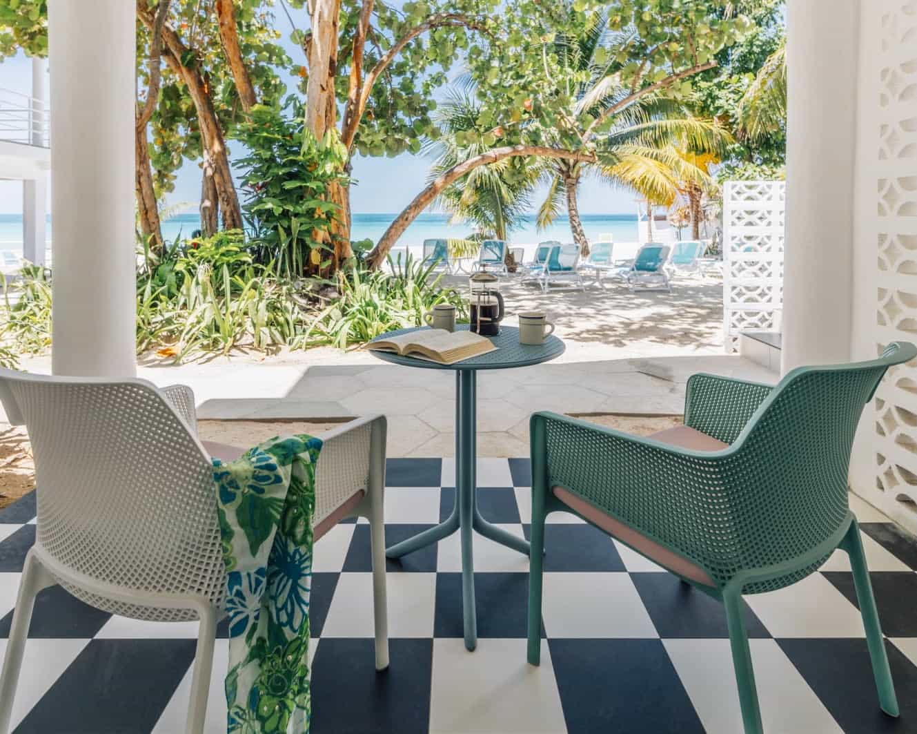 A patio view with chairs and small side table overlooking palm covered beach