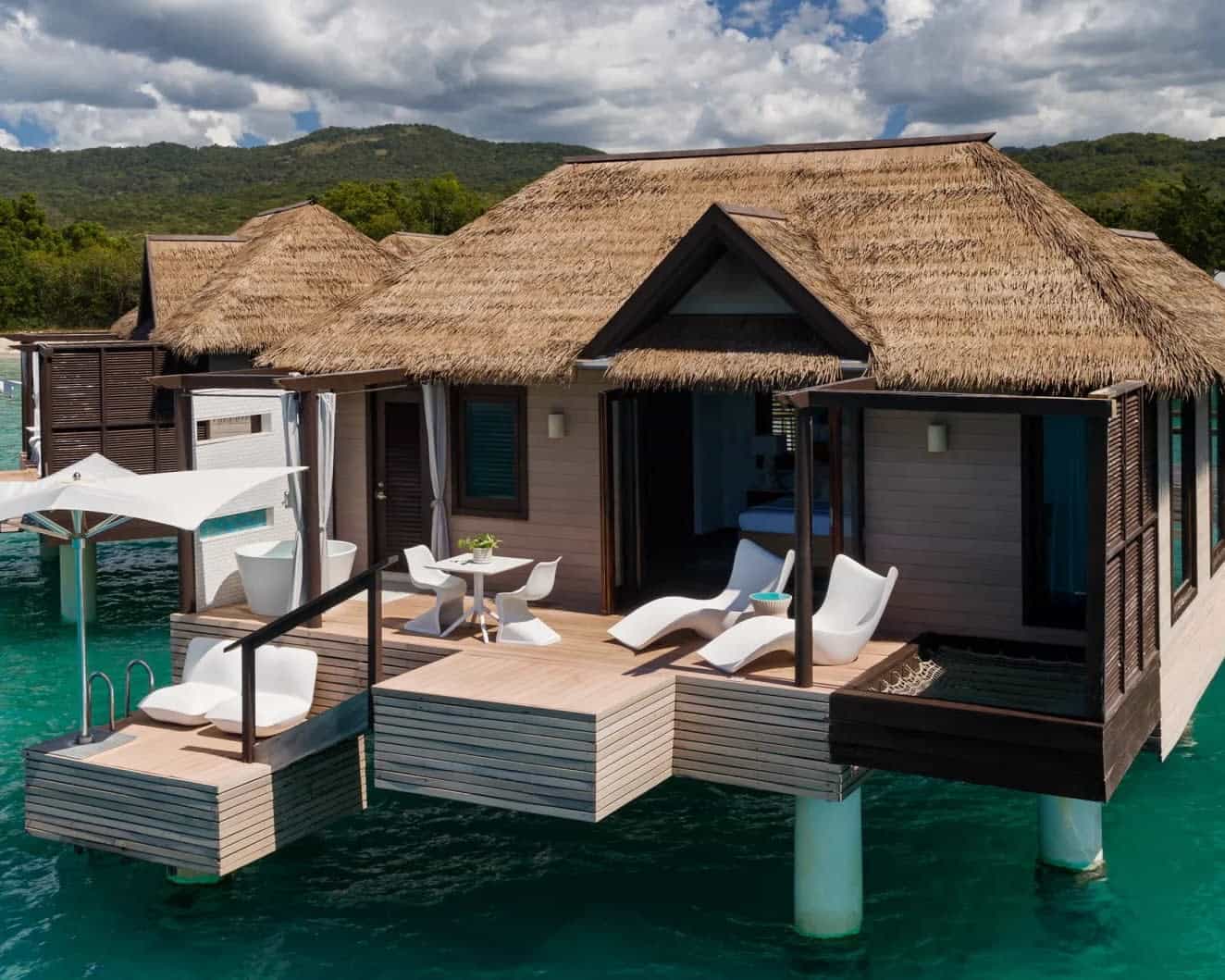 overwater bungalow with wood roof, wood decking, and white furniture over turquoise water during day