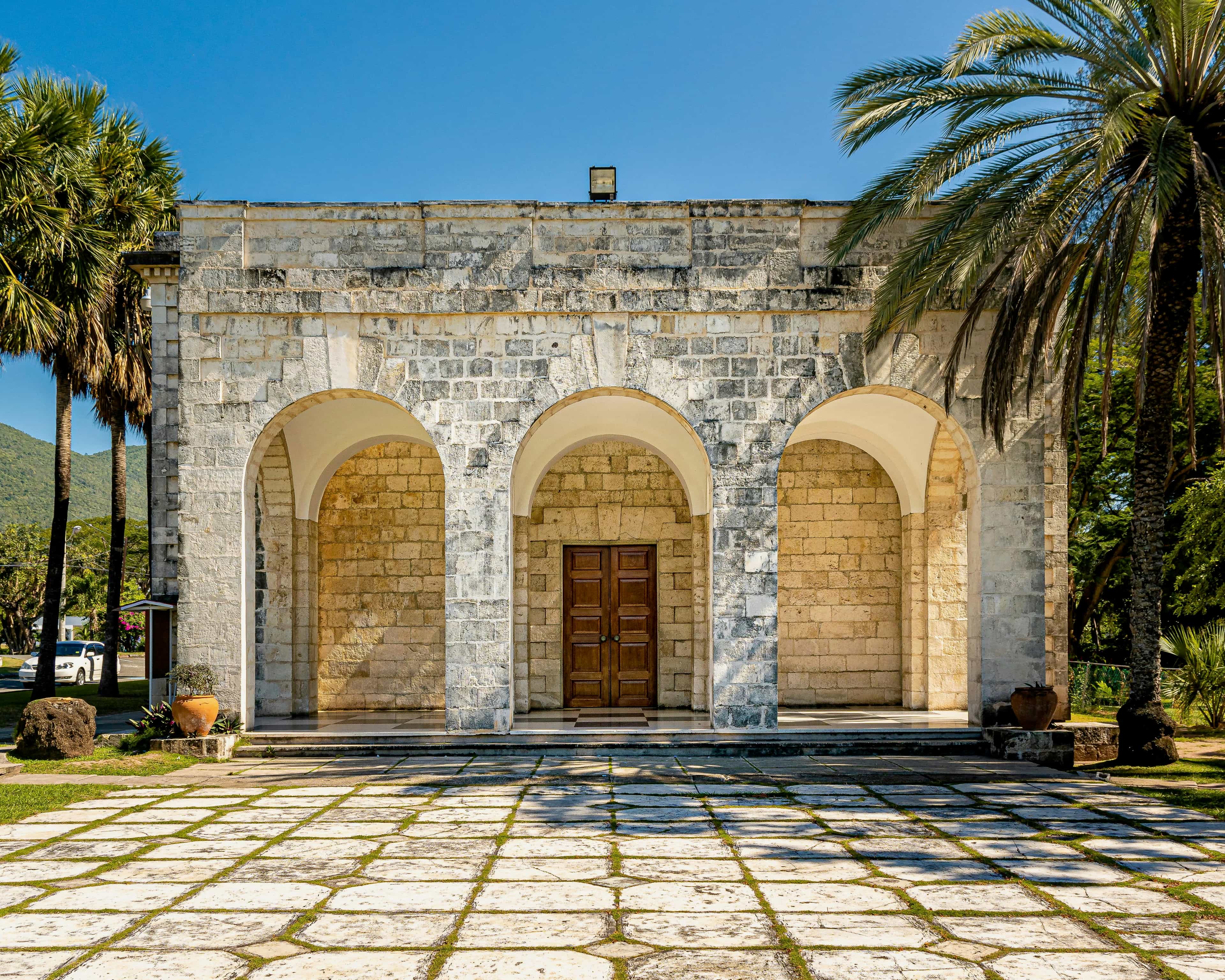 colonial style building with stone arches and courtyard with palm trees during day