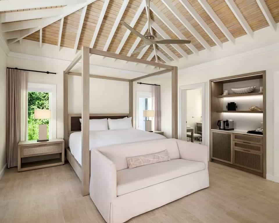 white vaulted wood beam ceiling, gray four poster bed, with white sofa at the foot of the bed.