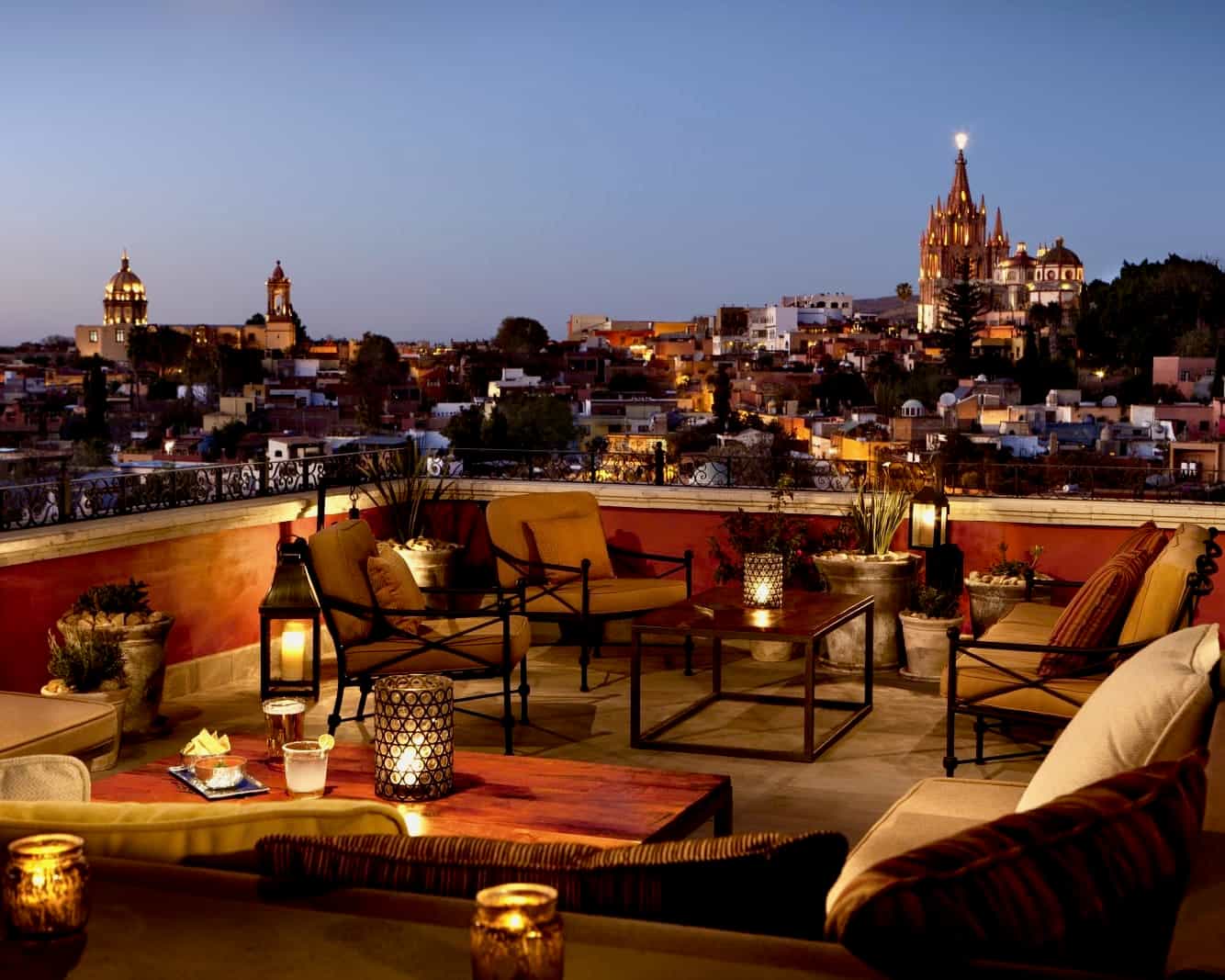 rooftop lounge with candles, tables and chairs at dusk with a cityscape in the background