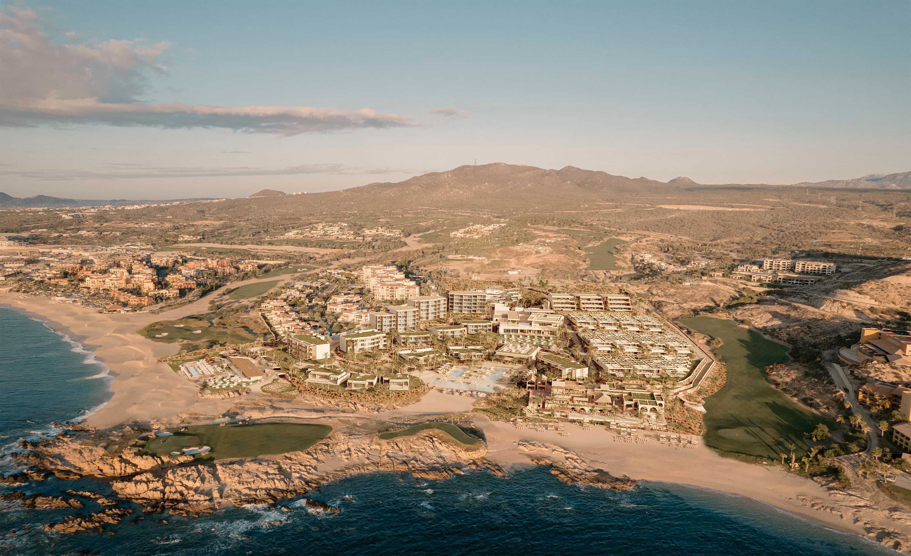 Aerial view of a luxury beachfront resort in Los Cabos, Mexico, surrounded by desert hills, a golf course, and the Pacific Ocean under warm golden light.