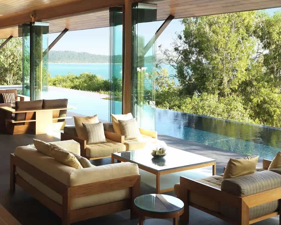 cushioned seating around a table with open windows to a pool, trees, and ocean