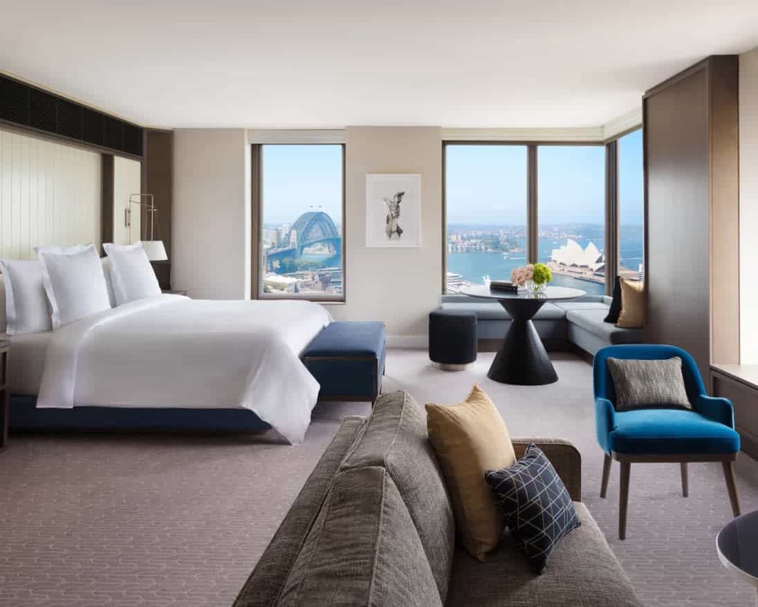 hotel suite with seating area and bed next to windows showing city landmarks outside