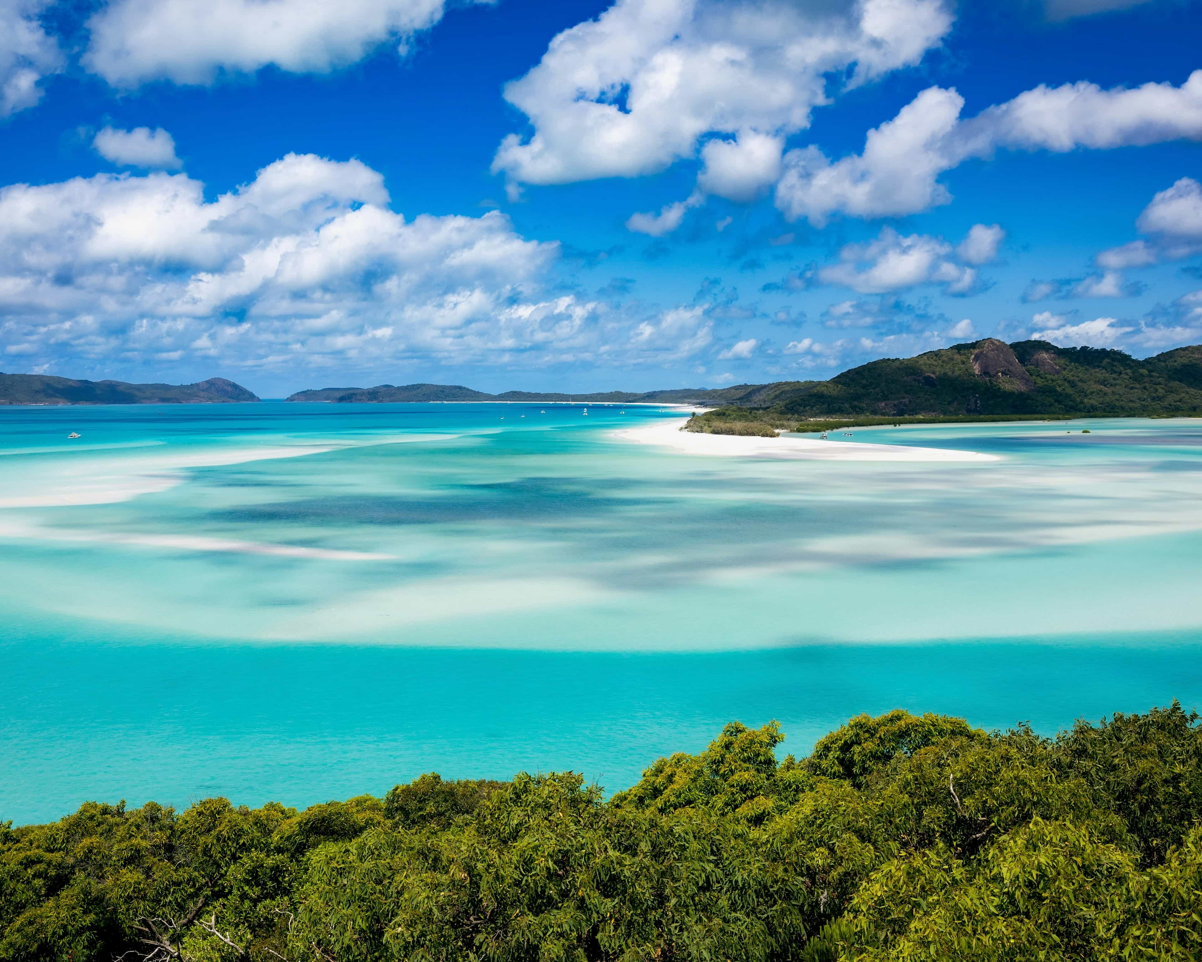 green mountains above turquoise waters with white sandbanks swirled throughout during day