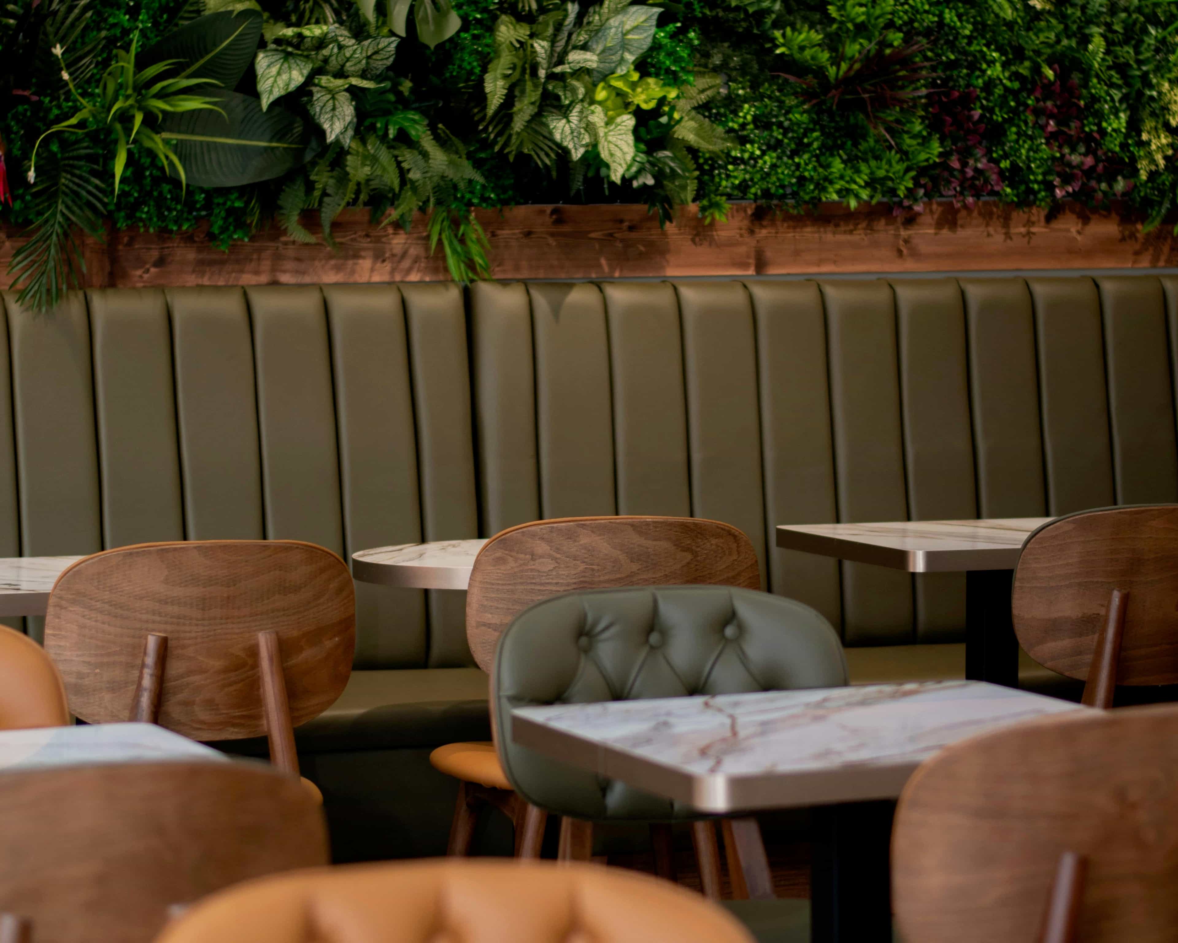 modern restaurant with green leather and tan wood seating, white marble tables, and green plant covered wall