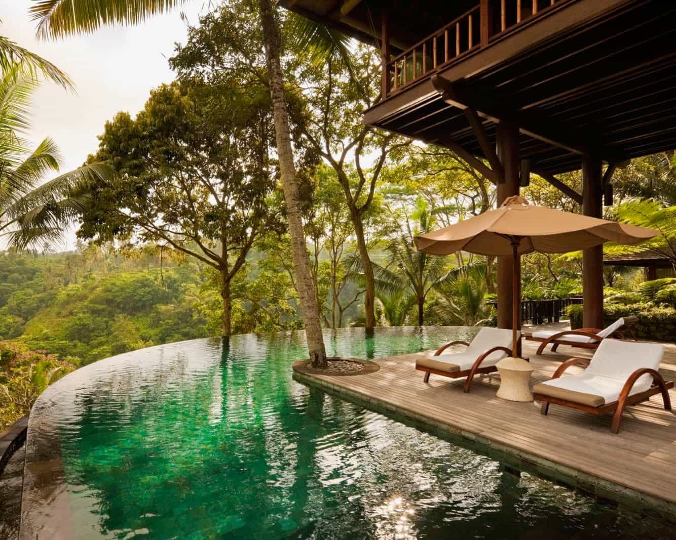 white lounge chairs next to a private pool under a wood cabin overlooking a green jungle during day
