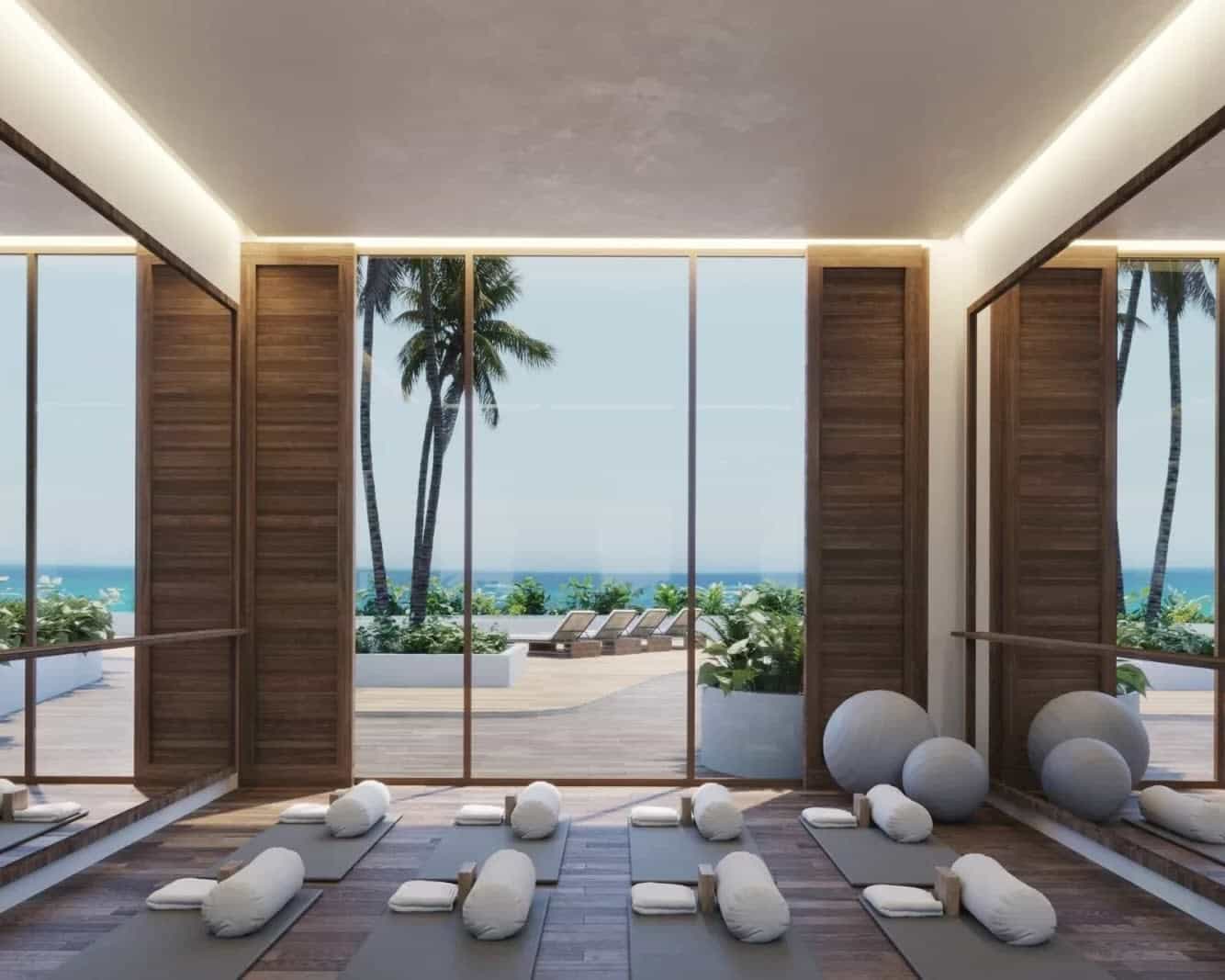 private yoga studio with mats overlooking a pool and beach during day outside floor-to-ceiling glass windows