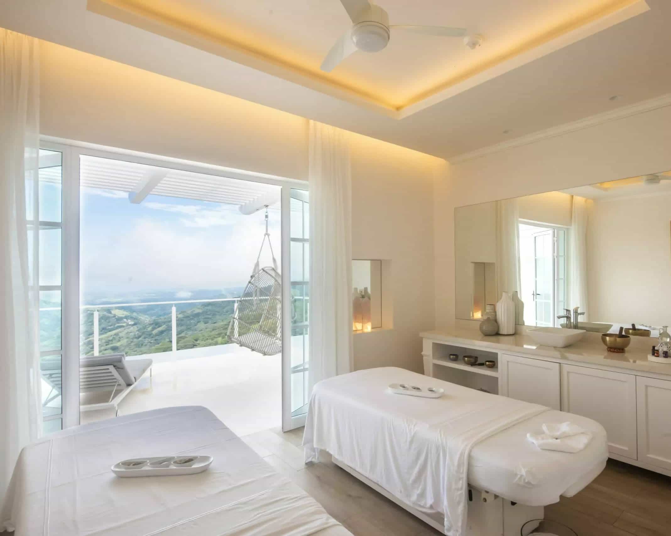 white sheet covered massage tables next to a balcony with chairs overlooking a green jungle landscap