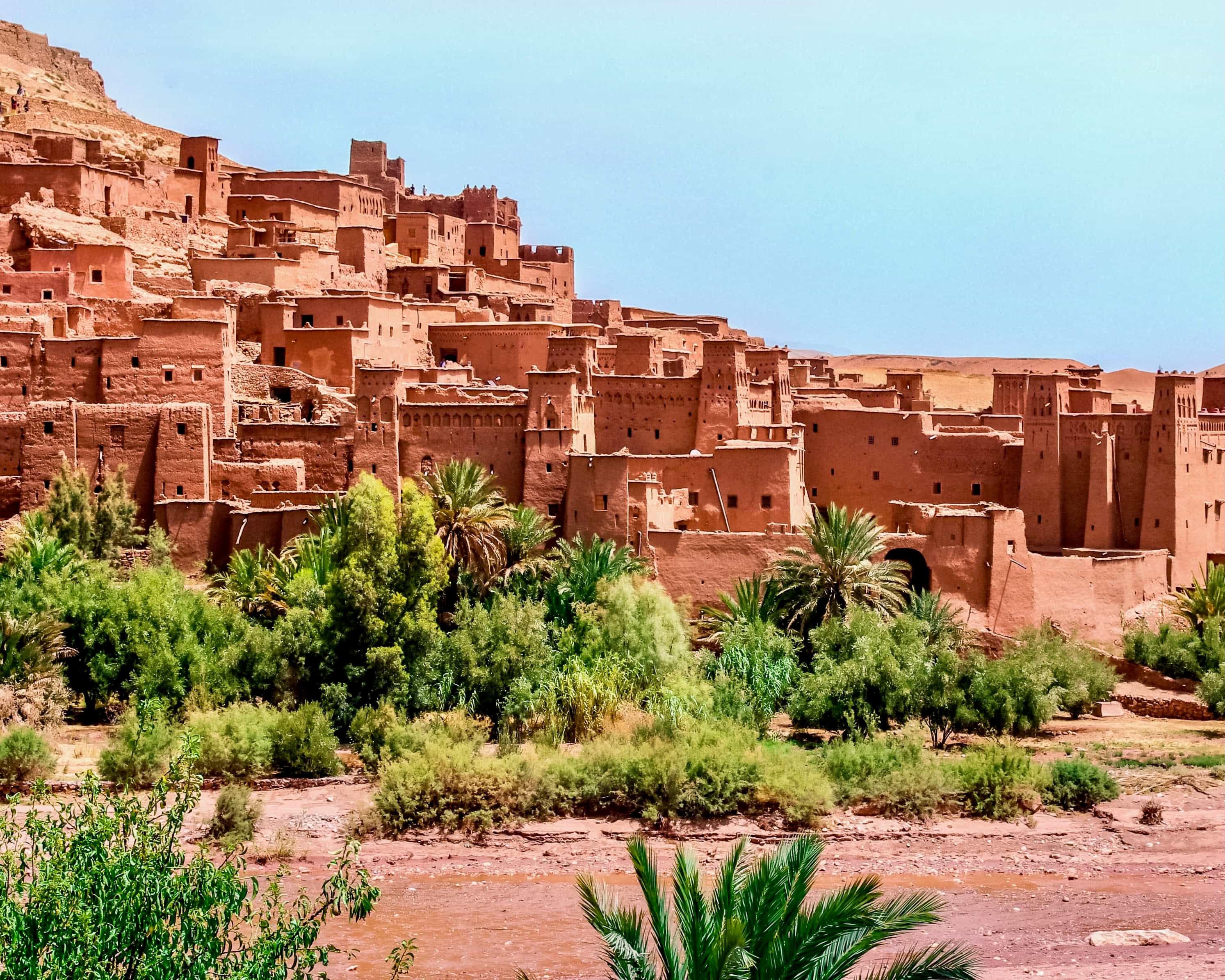 a historic tan walled city on the side of a hill next to palm trees
