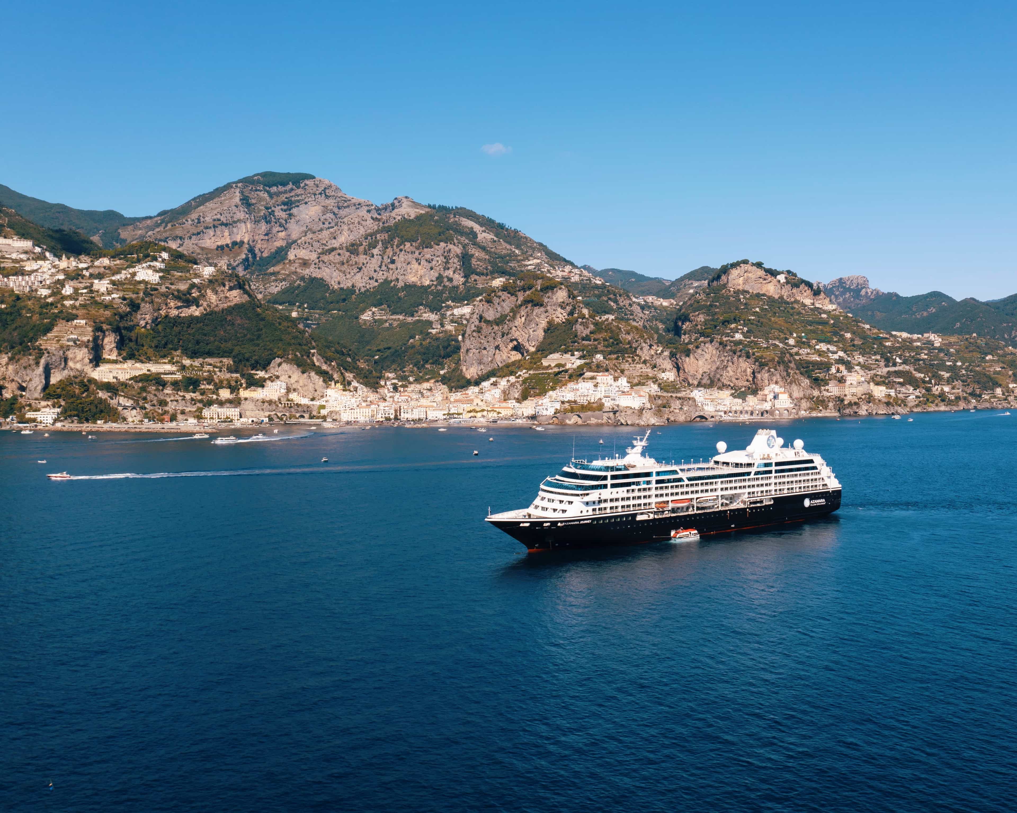 Cruise ship in turquoise waters off a green rocky hillside village