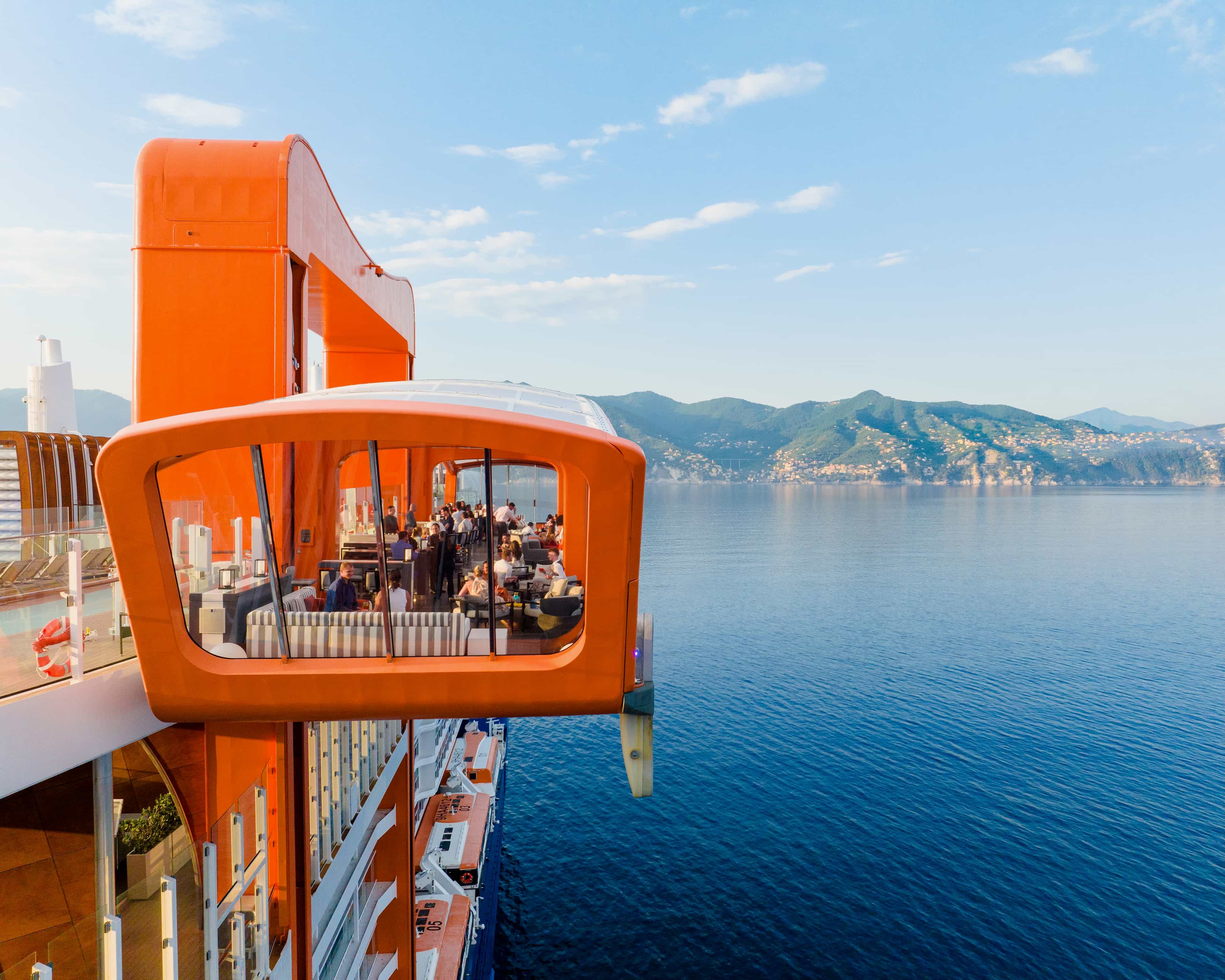 an orange restaurant deck off the side of a cruise ship off a hilly coastline during day