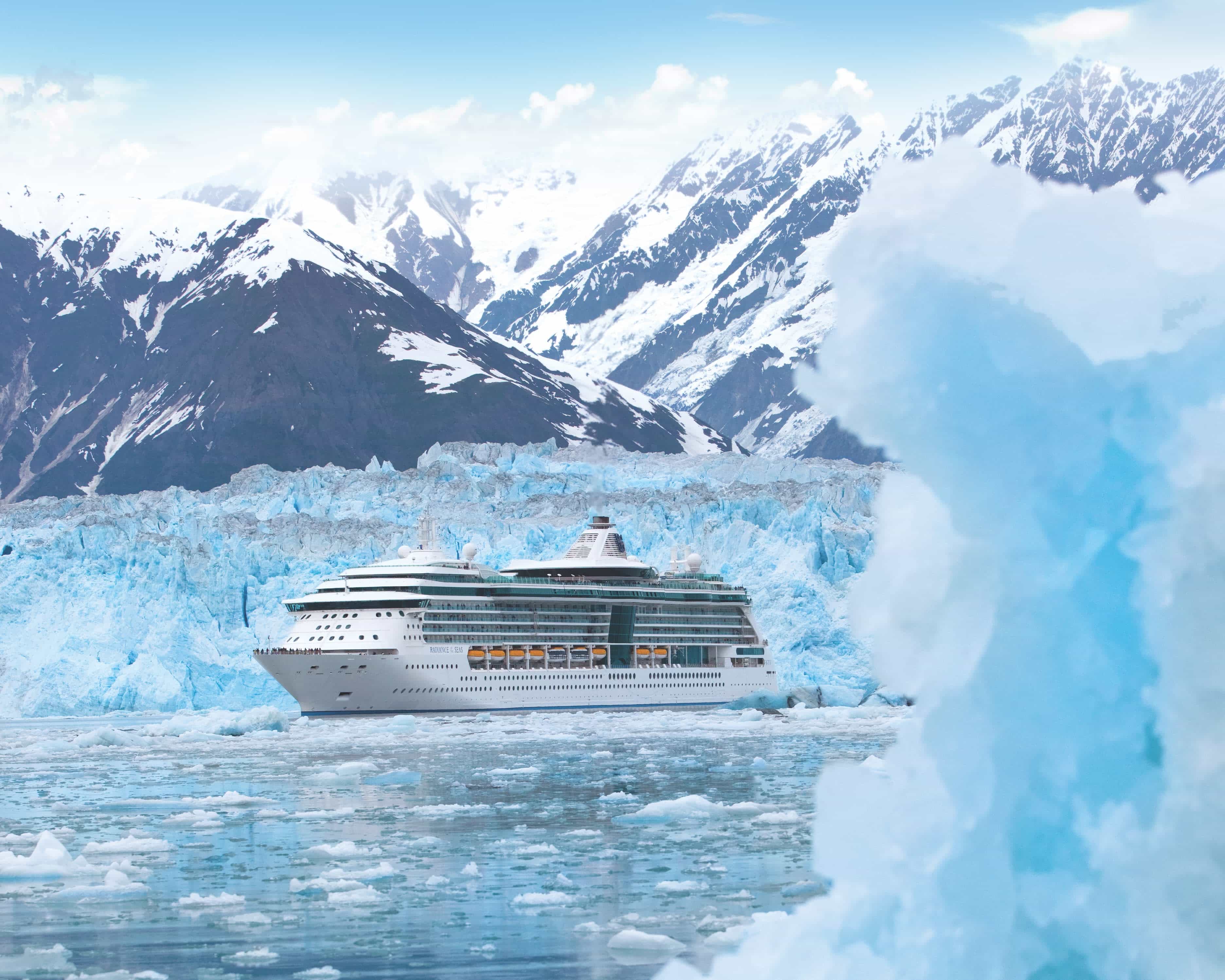 cruise ship in icy waters next to a glacier and snow capped mountain during day