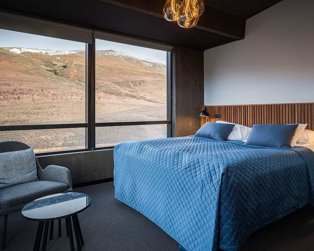 room with blue bed covers and grey walls with brown mountain outside