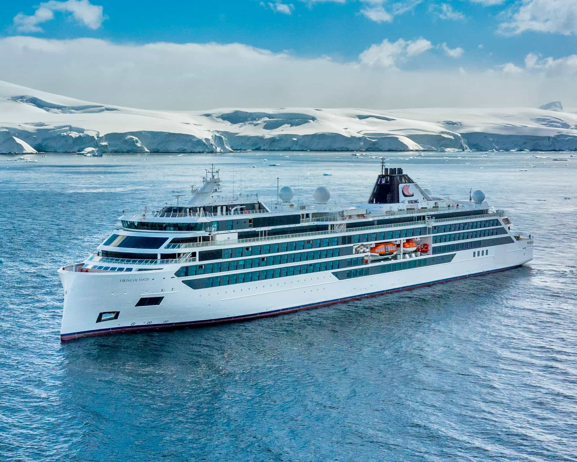 white expedition cruise ship at sea with snow covered cliffs during day in the background