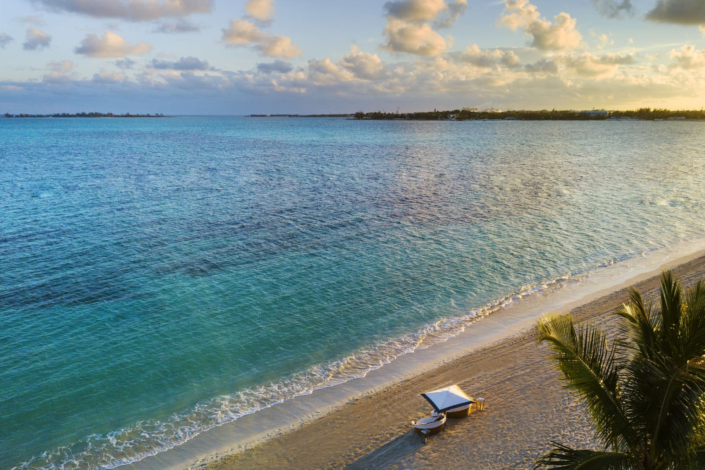 Sunset view of a beach with a lone cabana. The water is sapphire blue, and details on seafloor can be discerned