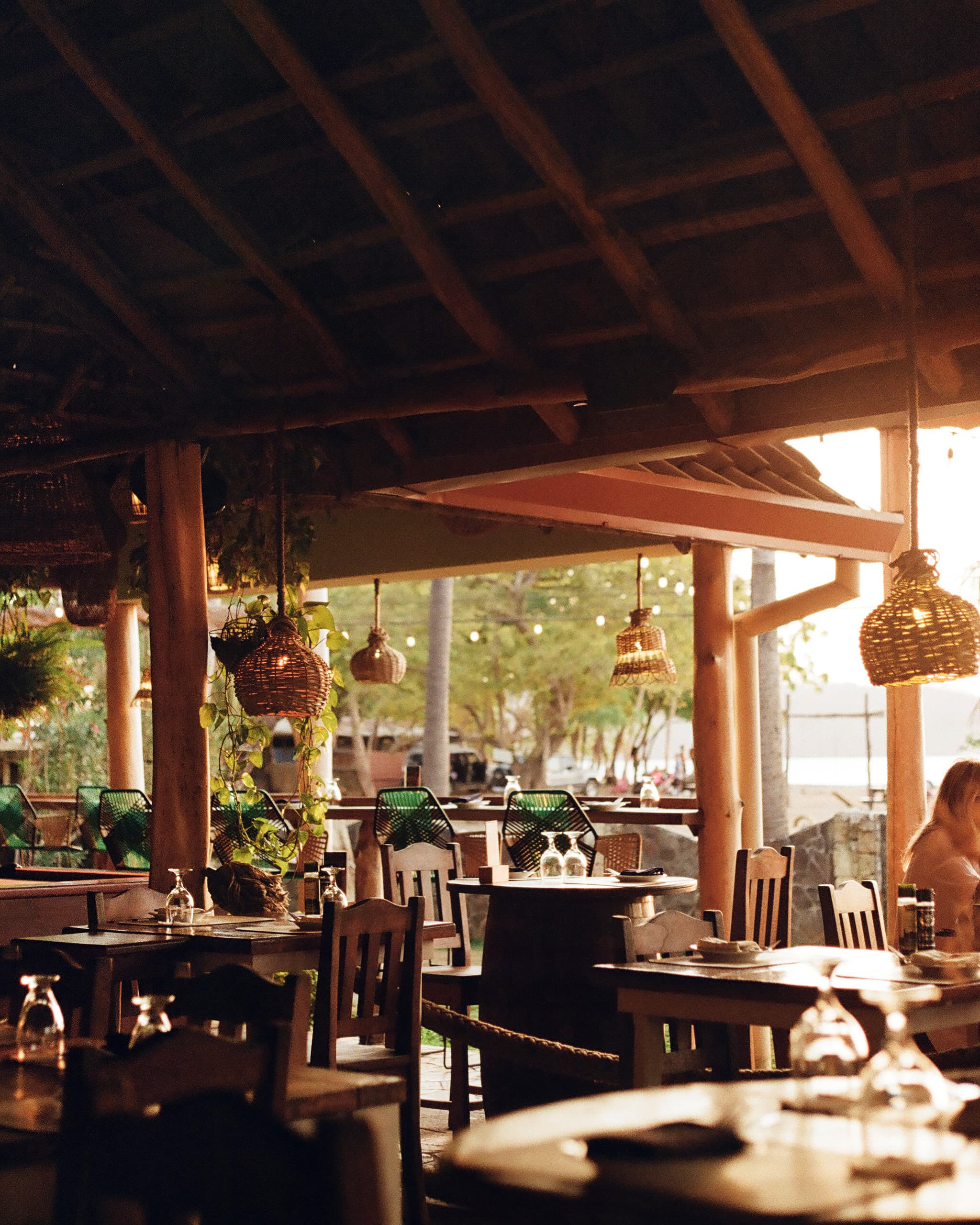 View of an empty outdoor restaurant with hanging lanterns and sunny views of water in the distance
