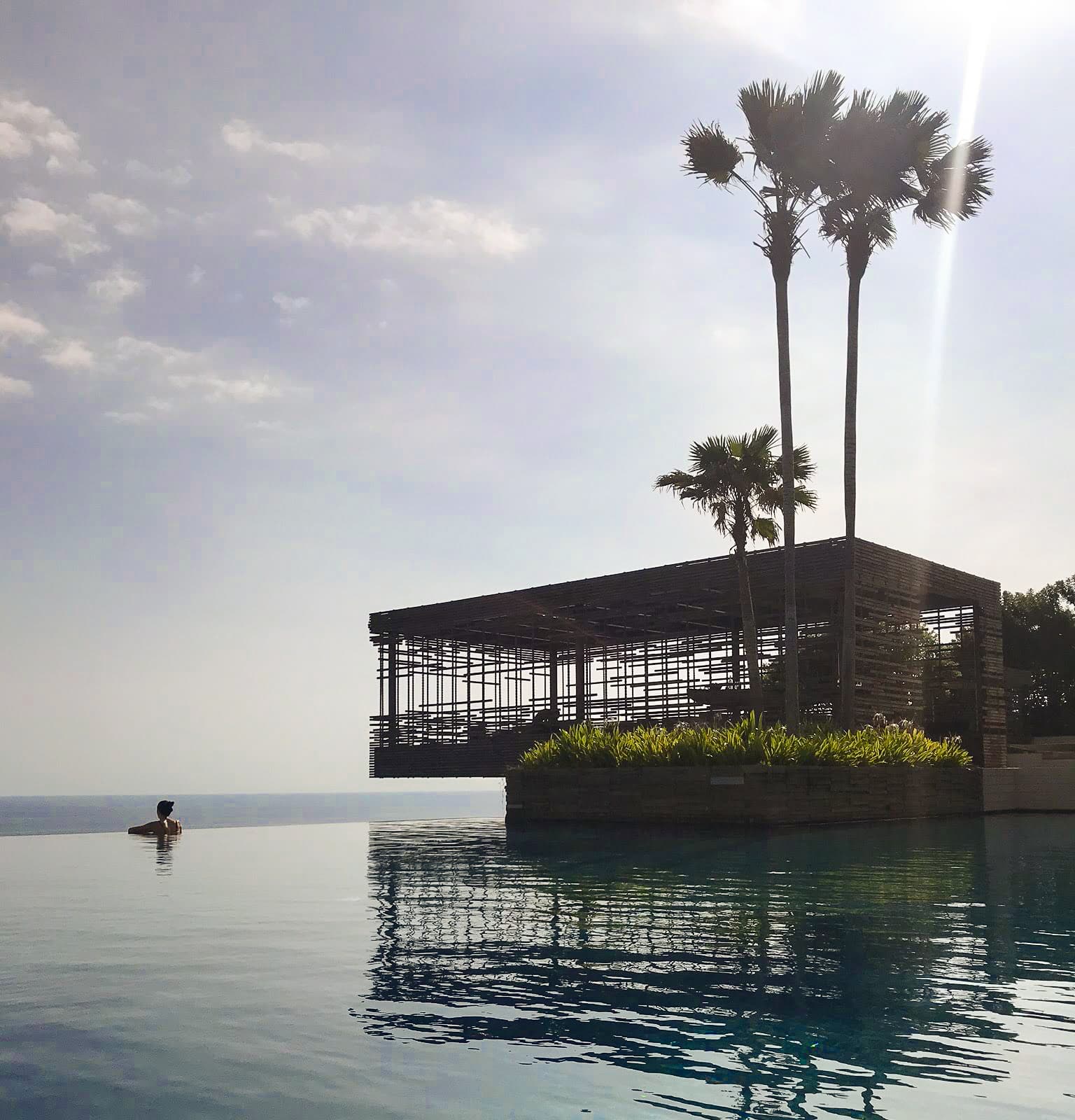 Beautiful view of a glass building and palm trees besides a large infinity pool stretching out to sea at Alila Uluwatu