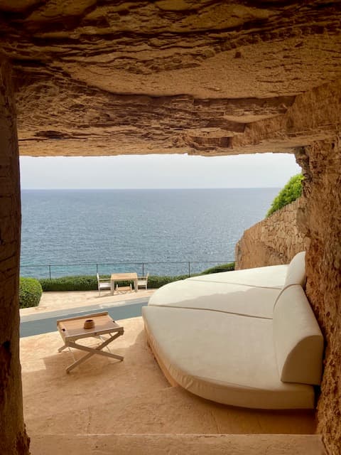 View of a white lounge bed besides a pool overlooking the sea on a sunny day