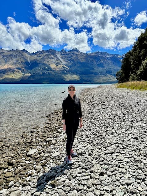 Advisor in all black standing on a rocky beach with a beautiful mountain range in the distance