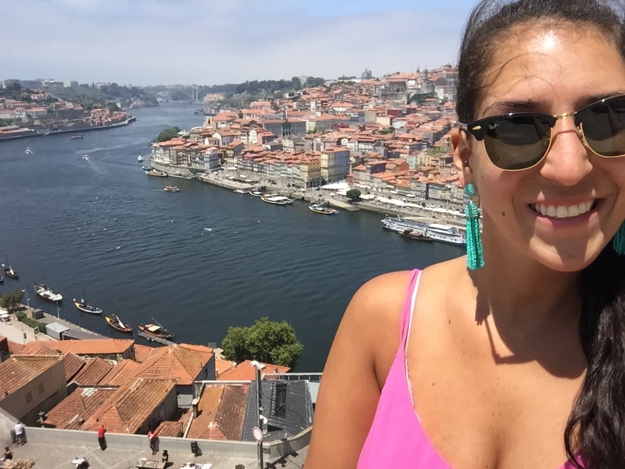 Lyndsay in a pink top and sunglasses taking a selfie with a beautiful city river view in the background