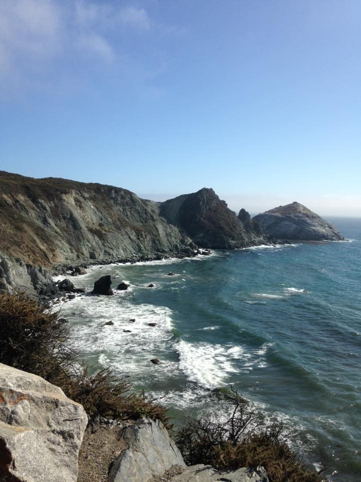 A view of the ocean during the day with large swells and a cliff in the distance.