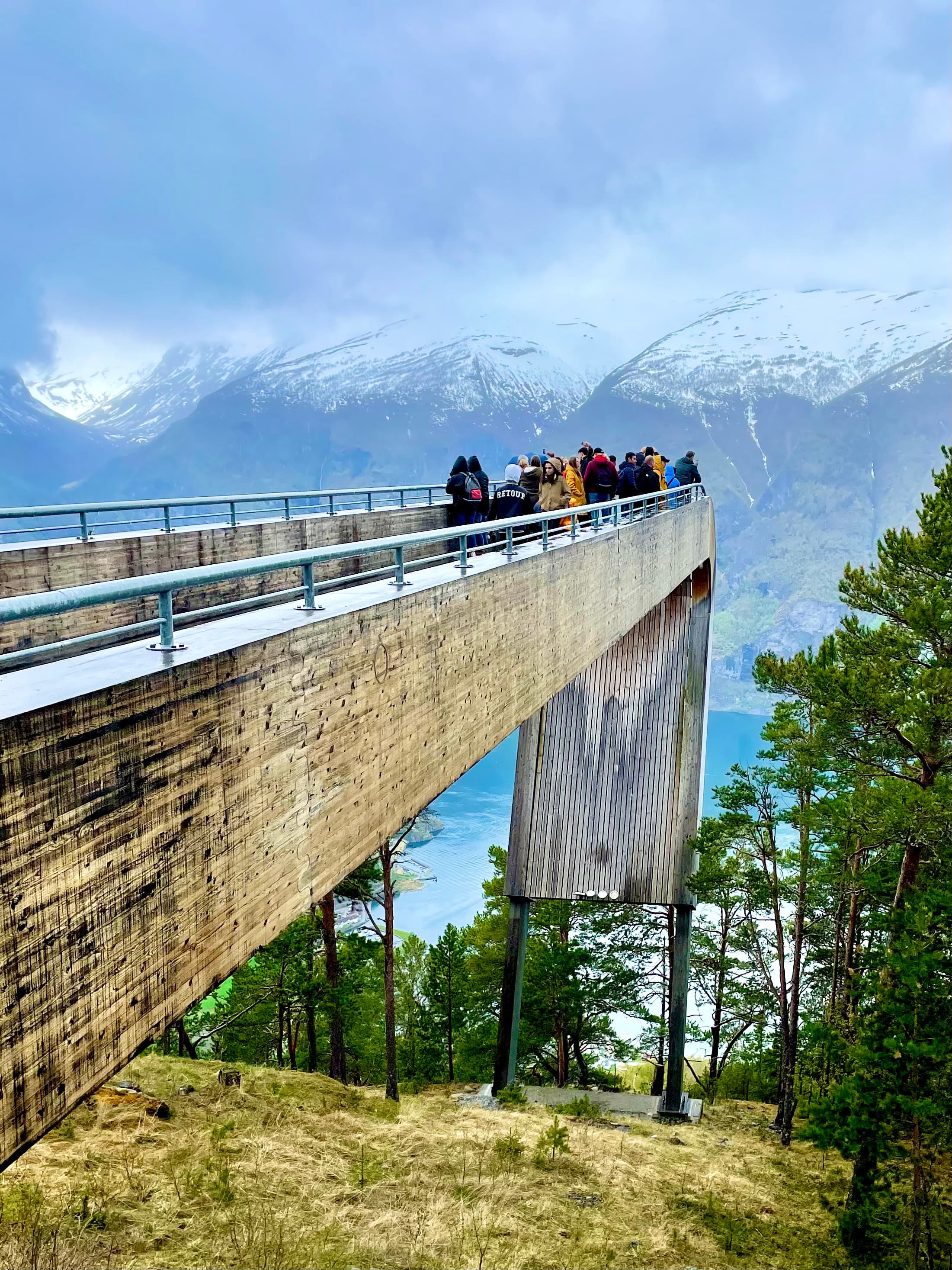A long, wooden bridge that extends into a body of water with foliage on a sunny day.