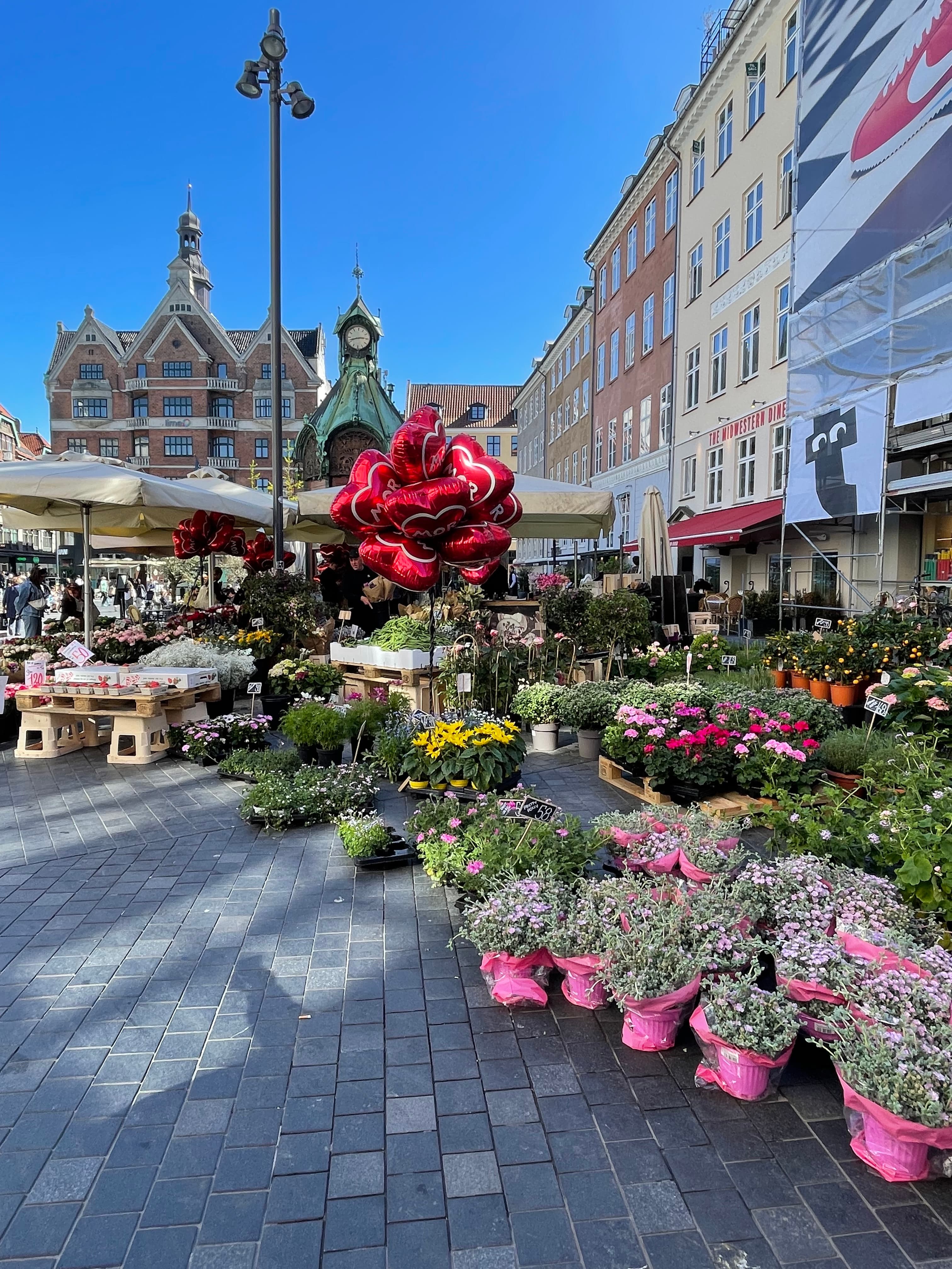 A flower market in a beautiful city square on a sunny day with buildings in the distance.