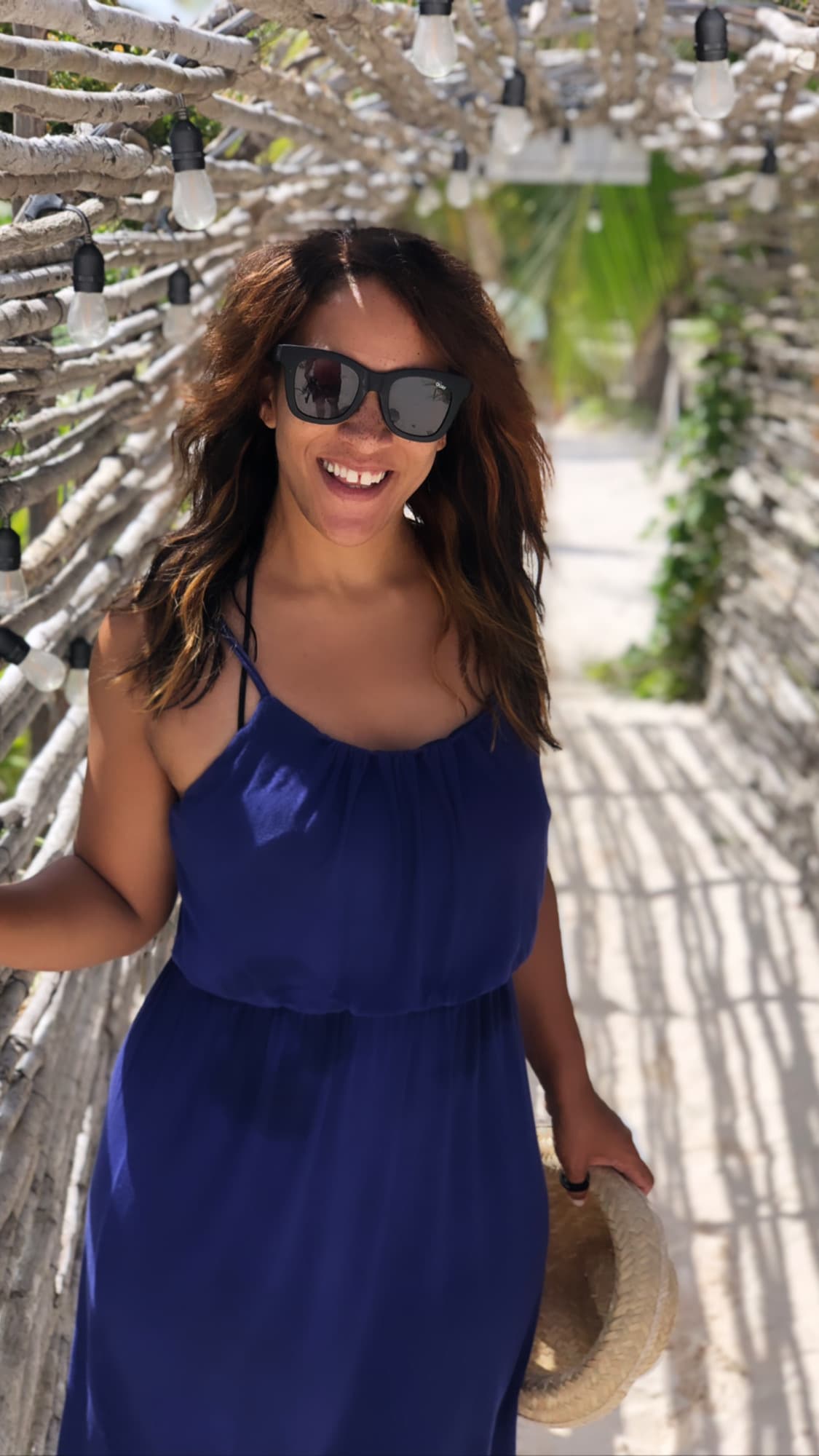 Advisor posing in a blue dress with a concrete alley and foliage in the distance.