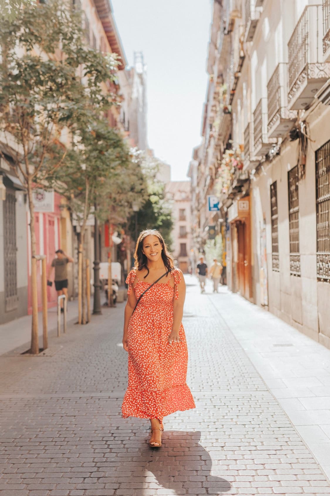 Advisor posing in an orange dress with a narrow street in the distance on a sunny day.