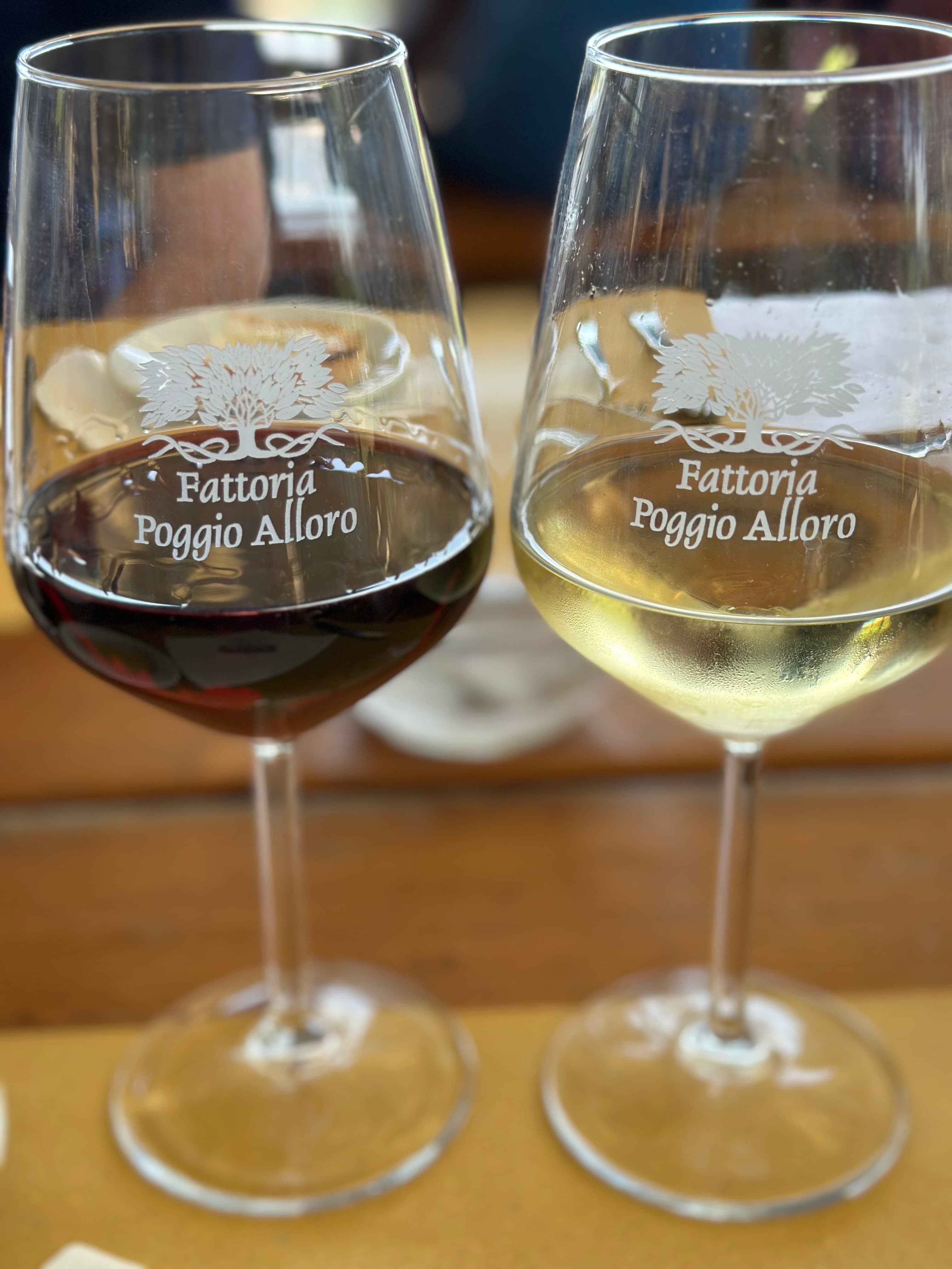 Two glasses of wine on a table with place settings in the distance.