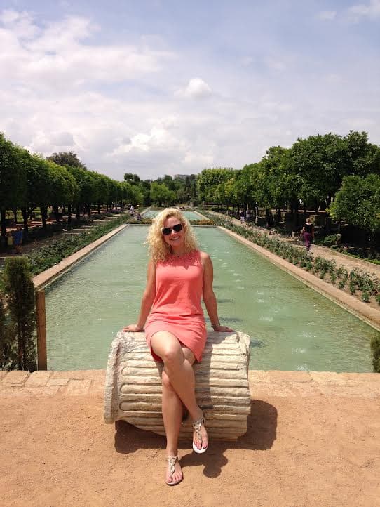 Travel advisor Meg sitting on a bench in front of a long, narrow body of water surrounded by gardens.