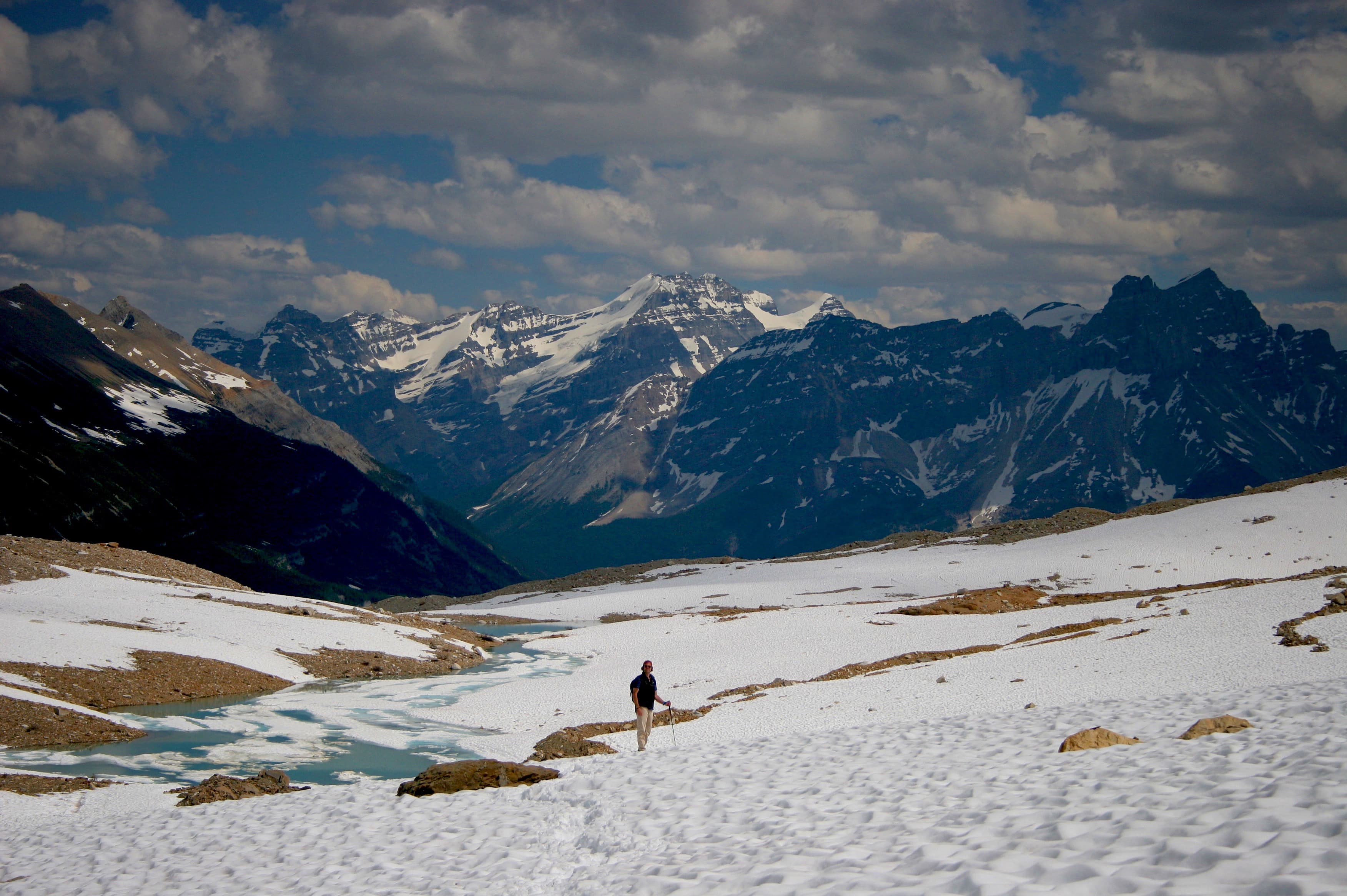 A snowy landscape with mountains in the background and a person walking.