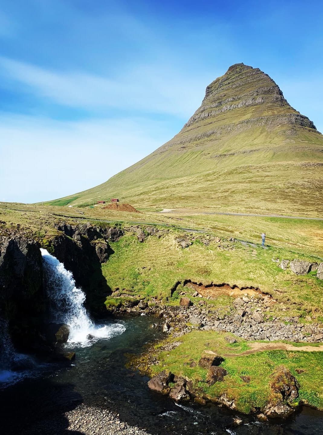 A green mountain next to a waterfall on a clear day in Iceland.