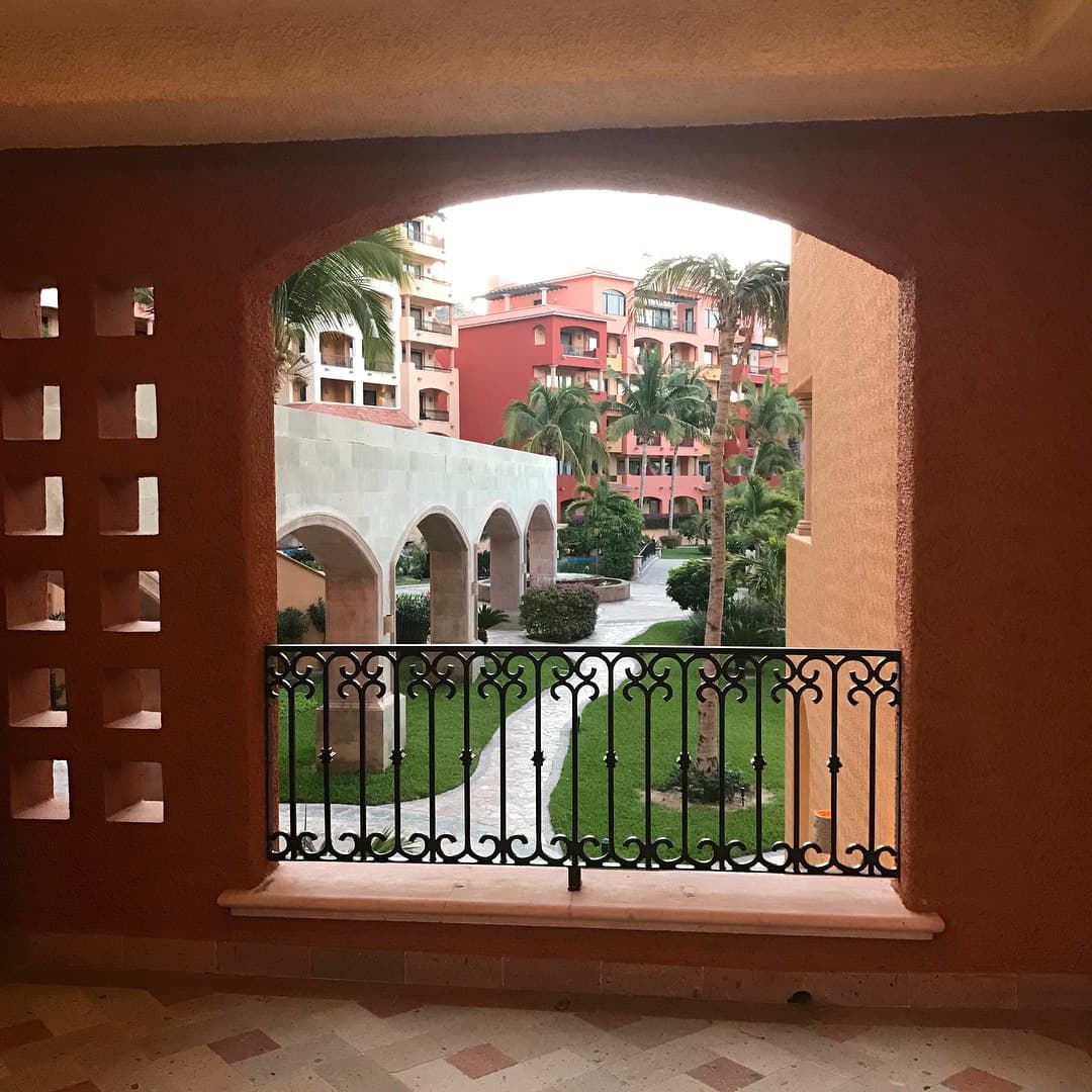 Hotel walkway overlooking a green lawn and red buildings.