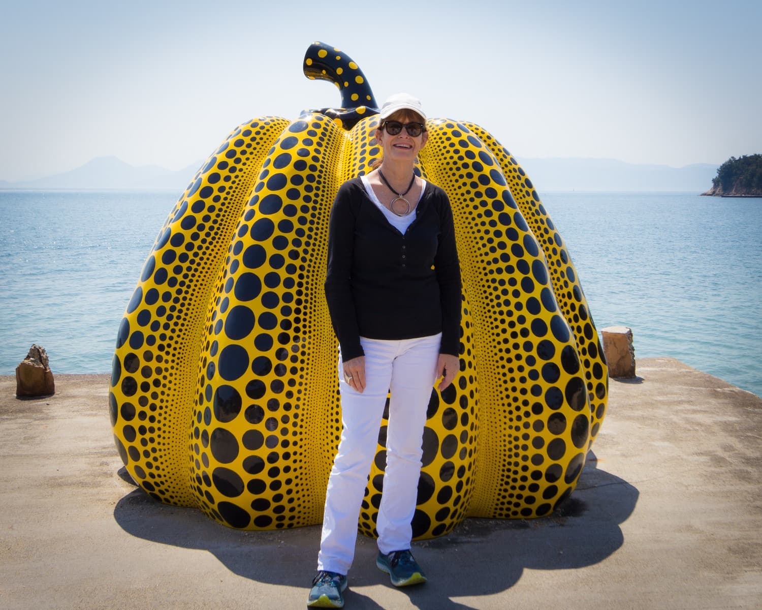 Nancy standing in front of a yellow Kusama pumpkin on a concrete dock.