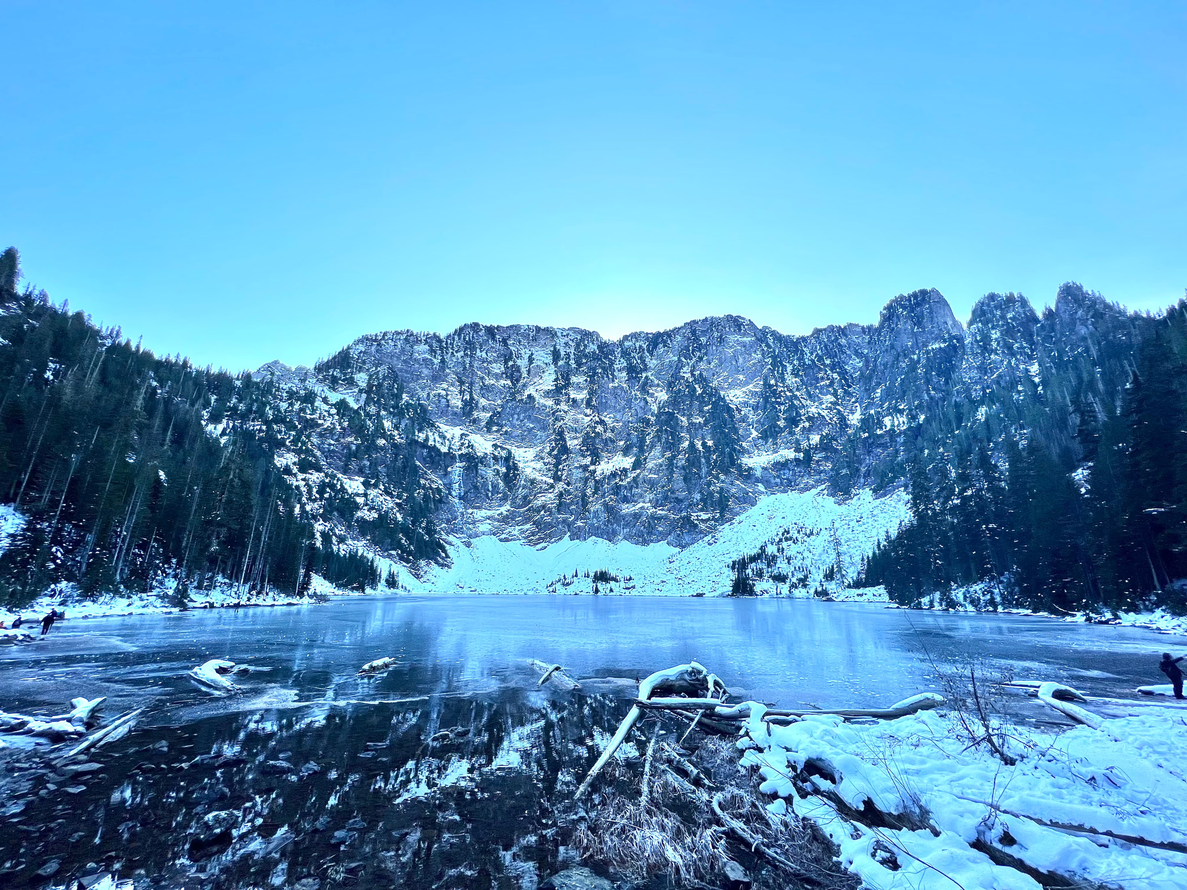 Snow covered mountains with an icy pond in the distance and trees surrounding the area.
