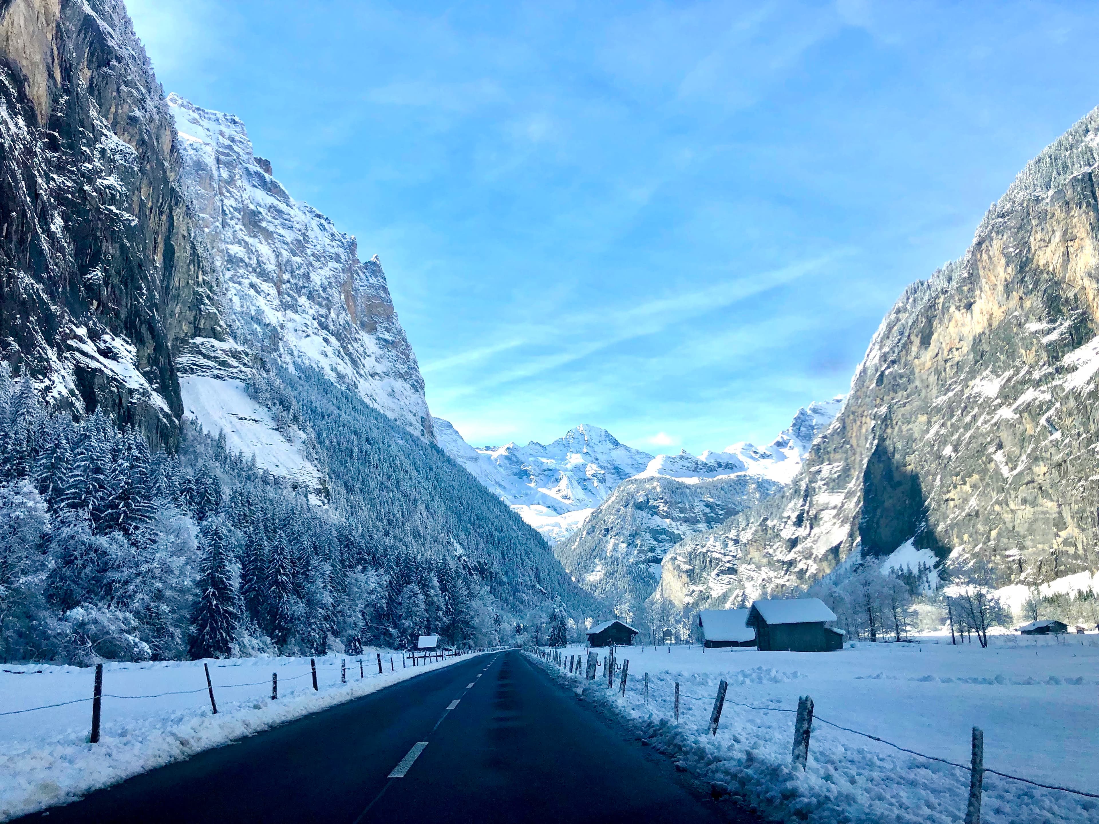 A snowy region with an empty road with large mountain scapes on each side.
