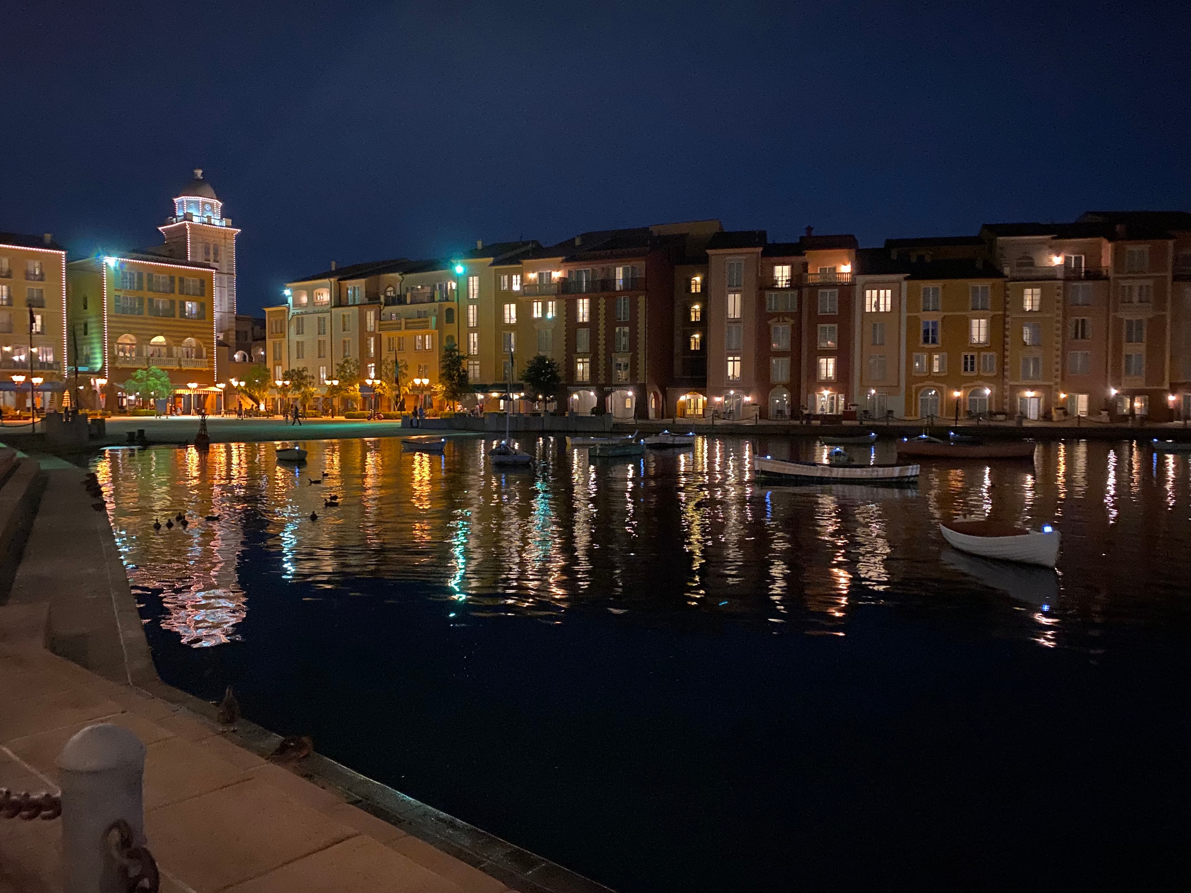 Pretty view of small boats floating in a bay at night with small buildings lit up in the background