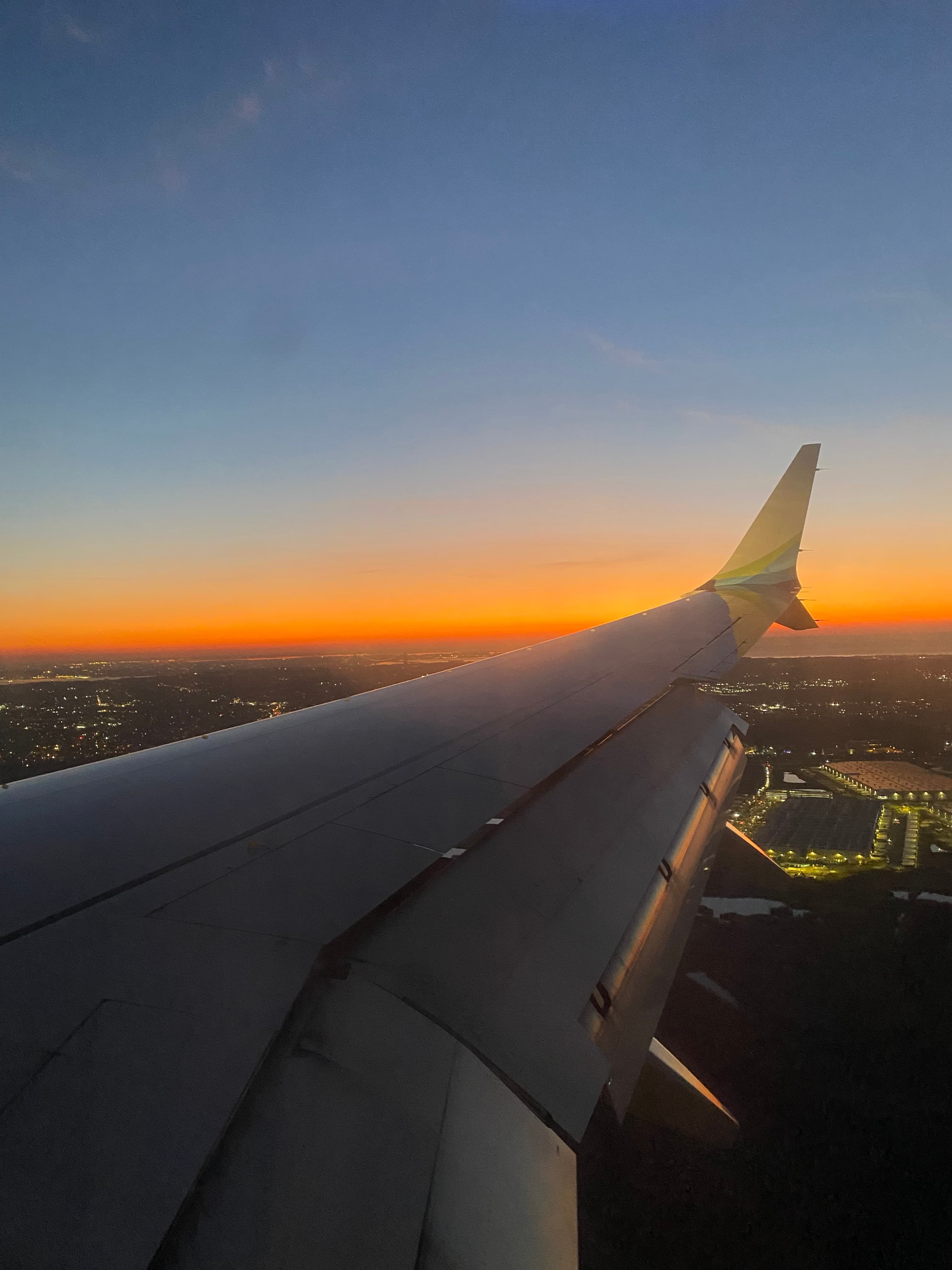 View of the wing of a plane in flight with an orange sunset on the horizon