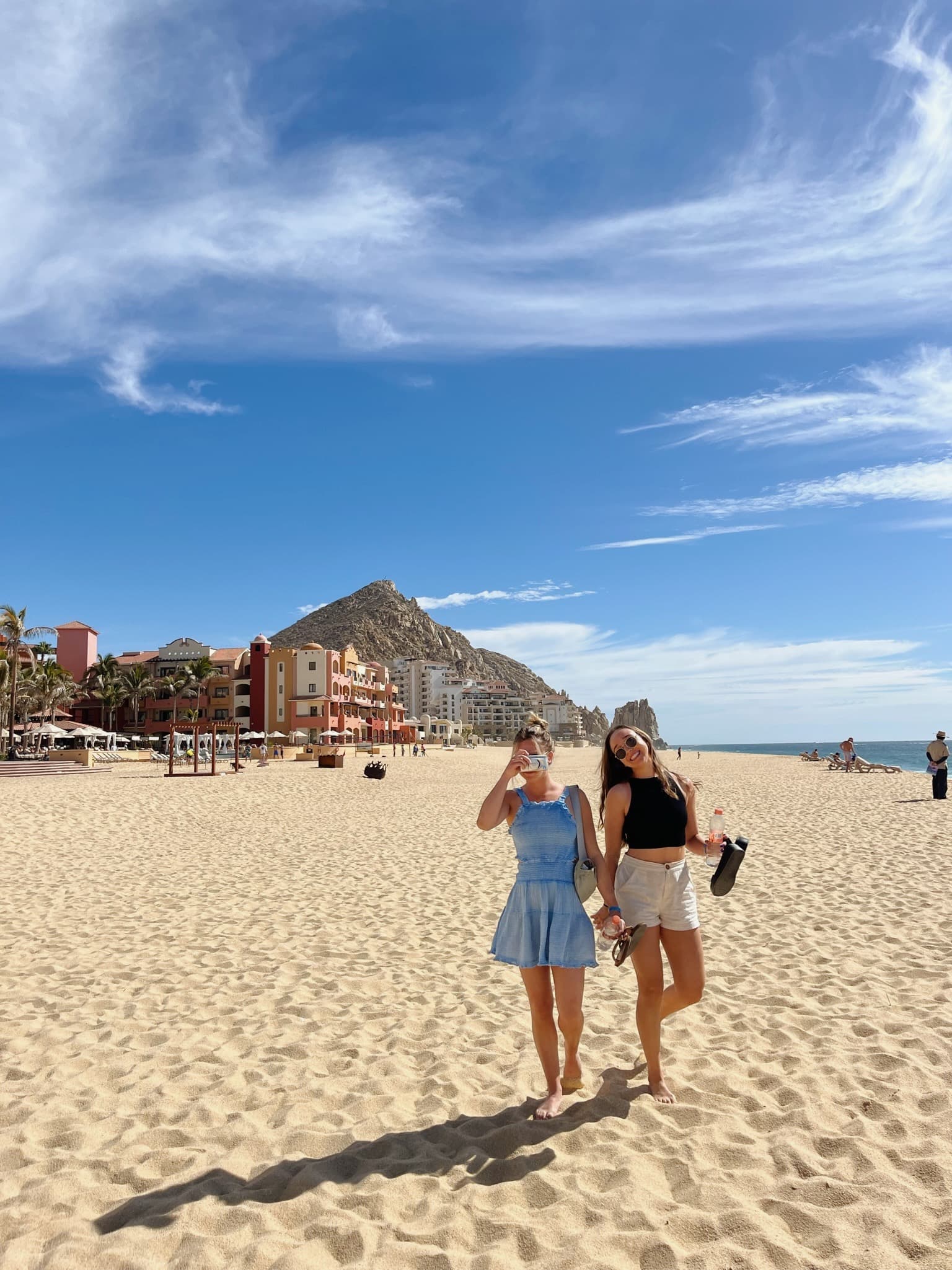 Advisor posing for a photo with a friend on a sandy beach with mountains in the distance on a sunny day.