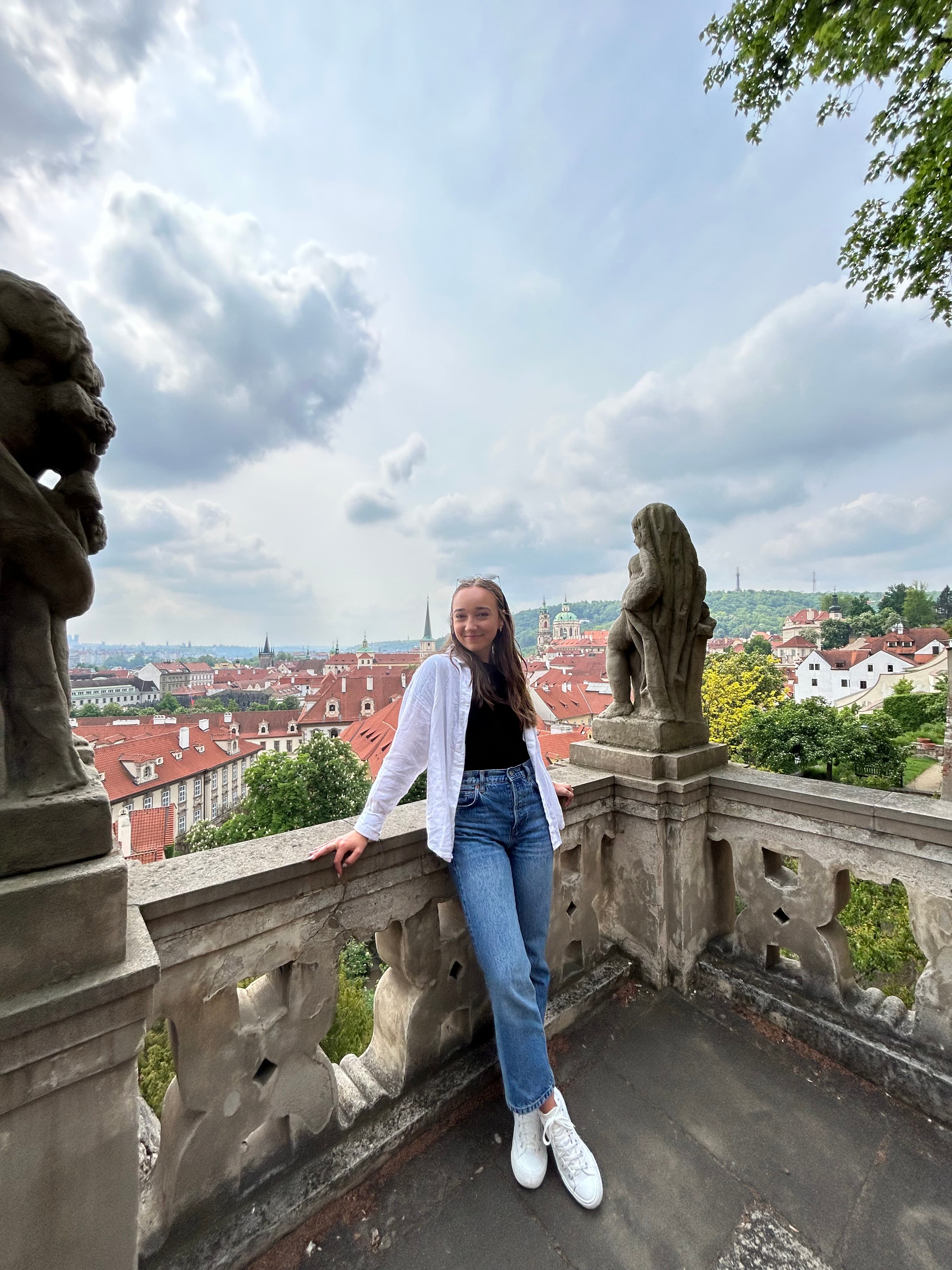Advisor posing for an image on a classic concrete balcony with statues and a city in the distance on a cloudy day.