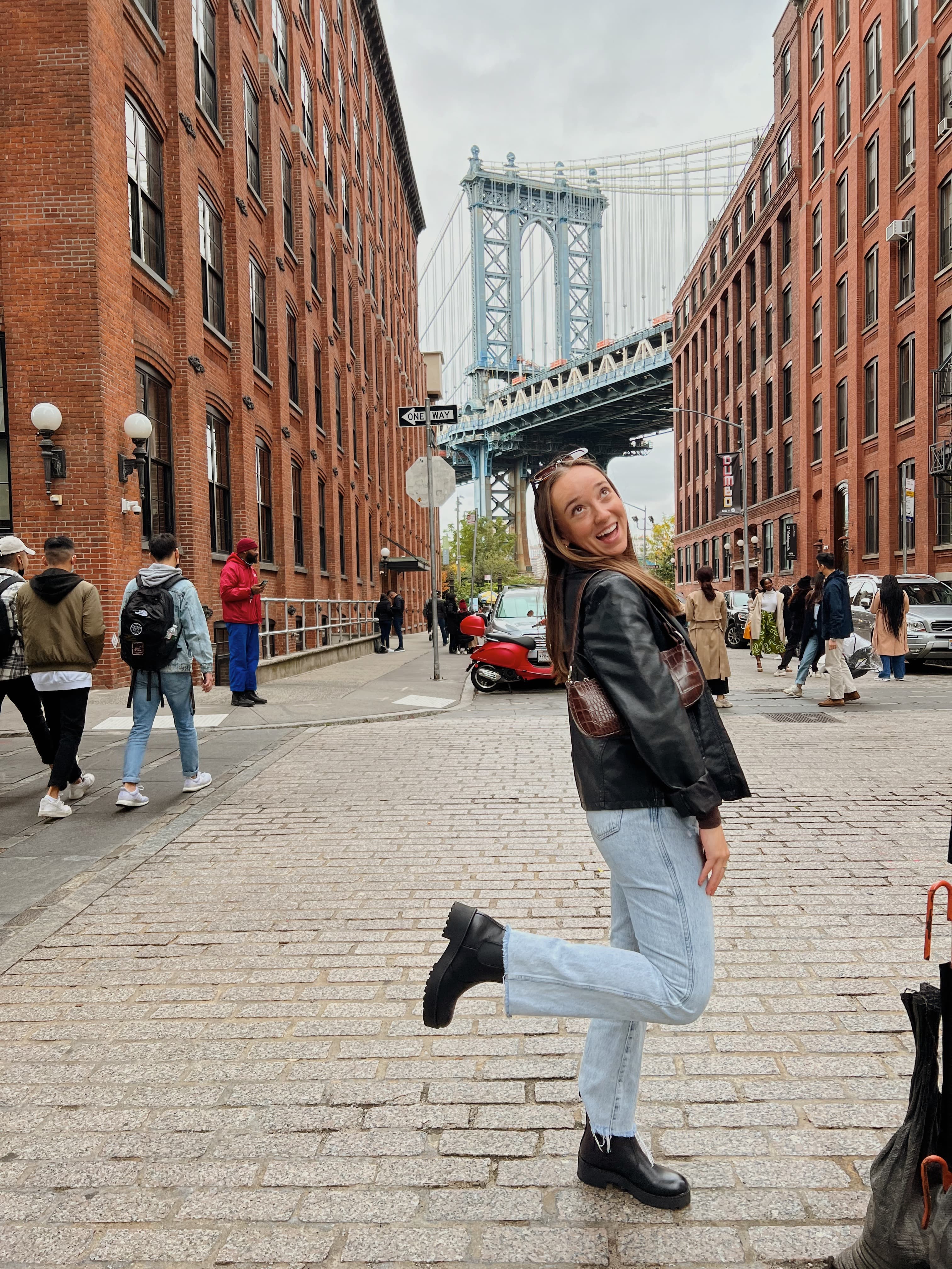 Advisor posing for an image in Brooklyn with the bridge in the distance on a cloudy day.