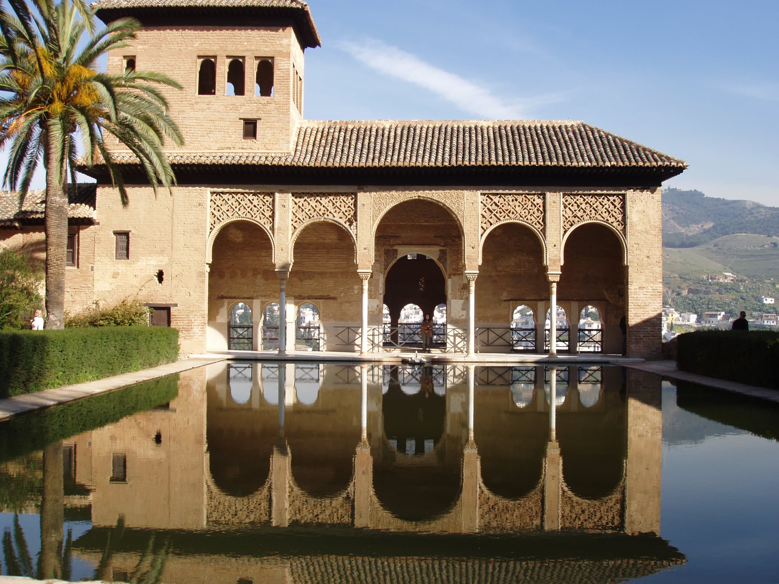 Image of a lovely pool with a hotel that has large arches and a tile roof.
