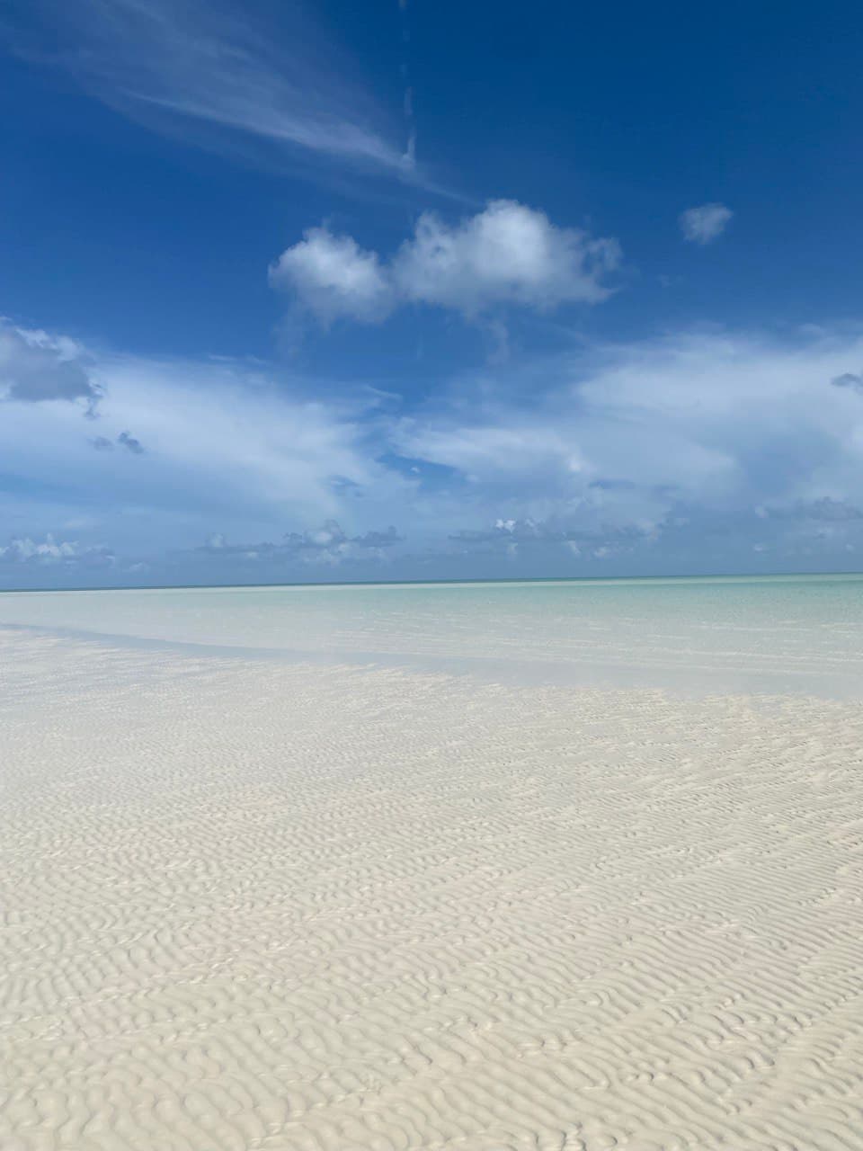 View of an empty white sand beach with crystal clear water stretching to the horizon a clear day