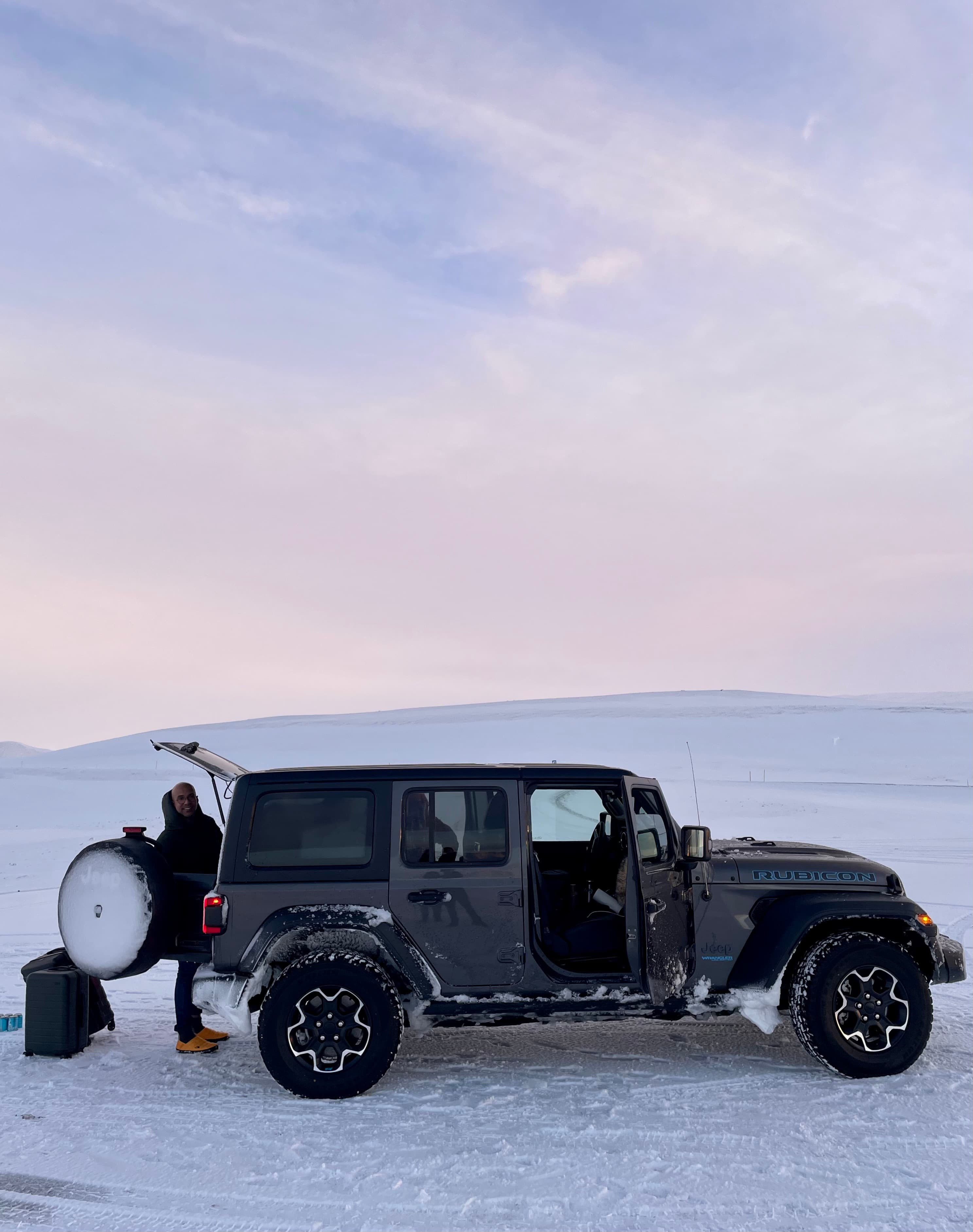 View of a jeep with the front door open parked in the middle of an icy landscape