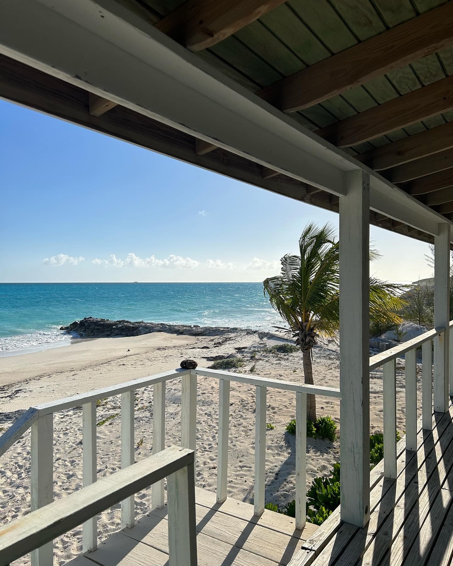 Beautiful view of a white-sand beach and sparkling ocean seen from a wood porch on a sunny day