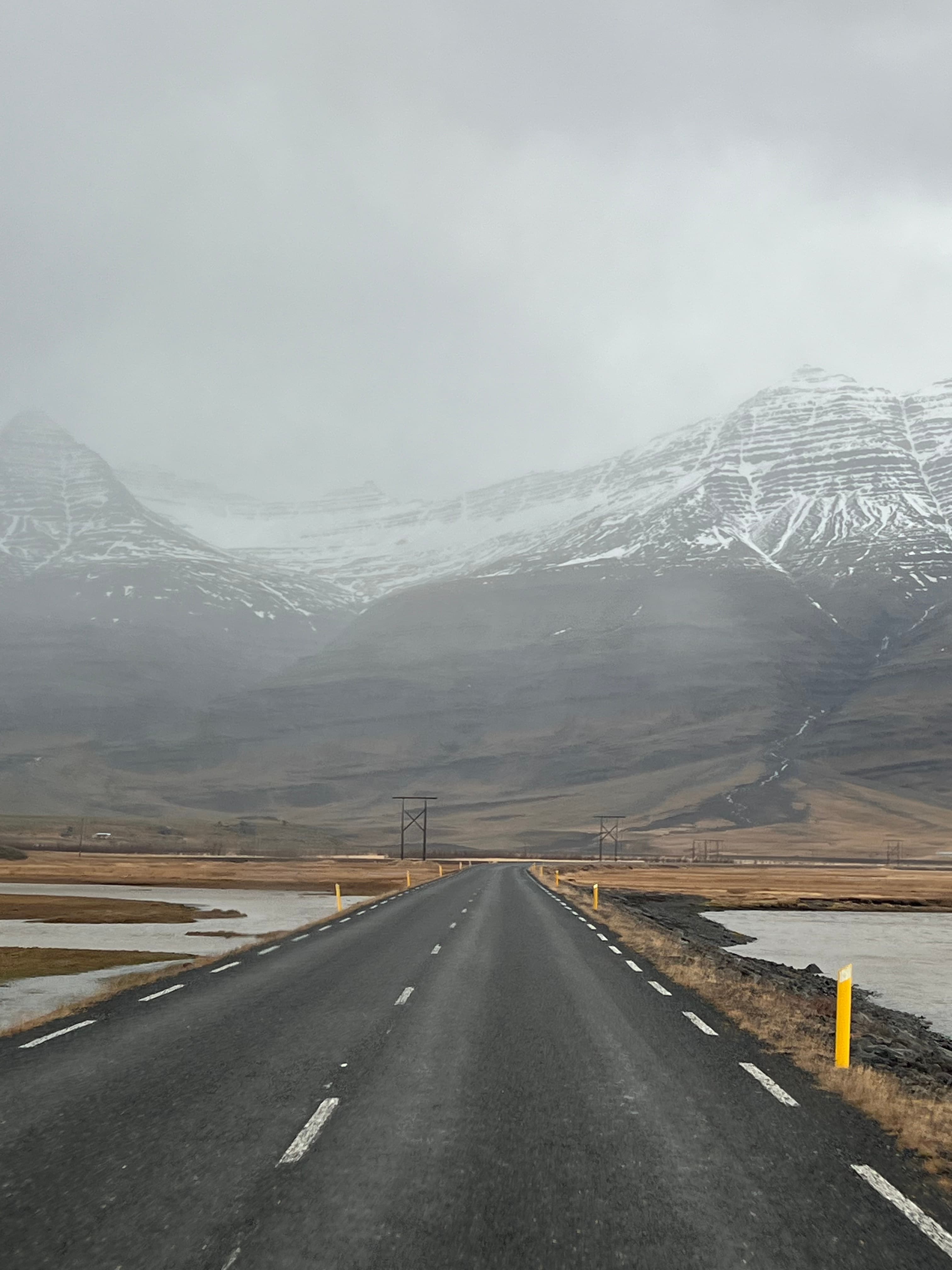 View of an empty road leading towards large snowy mountains slightly covered in clouds