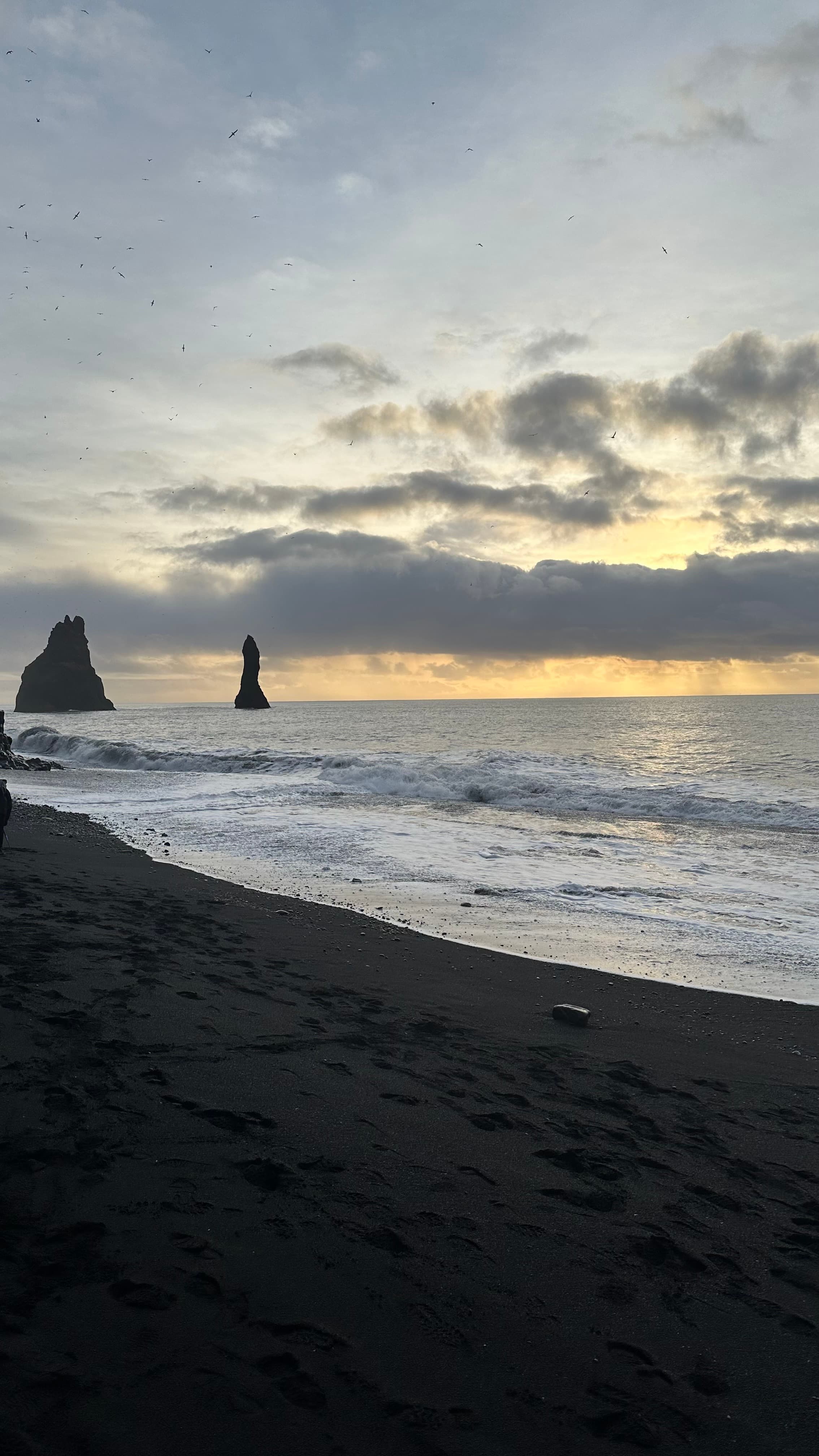 View of waves onshore the beach at sunset with rock formations seen in the distance