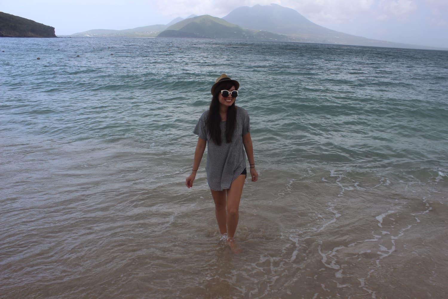 Imagine of Michelle wearing a hat and sunglasses while standing in shallow ocean on a cloudy day